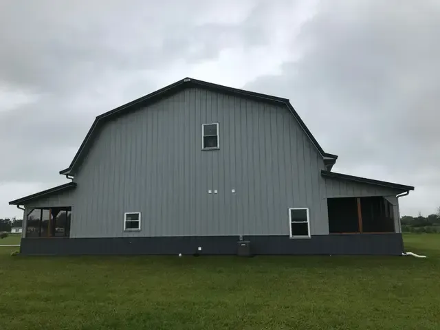 A large barn with a screened in porch is sitting in the middle of a grassy field.