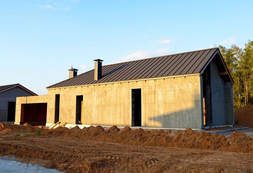 A concrete house with a metal roof is being built in a dirt field.