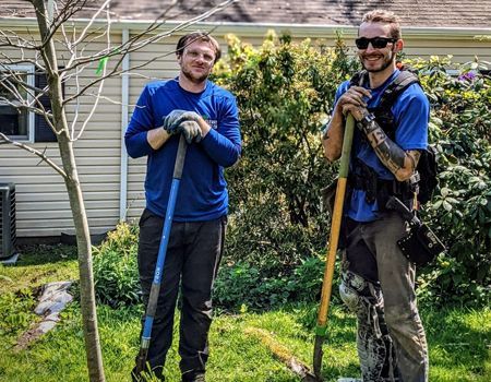 Two men are standing next to each other in a yard holding shovels.