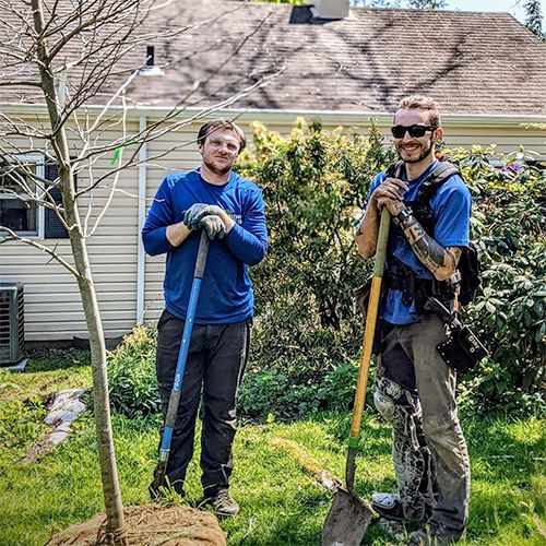 Two men are standing next to each other in a yard holding shovels.