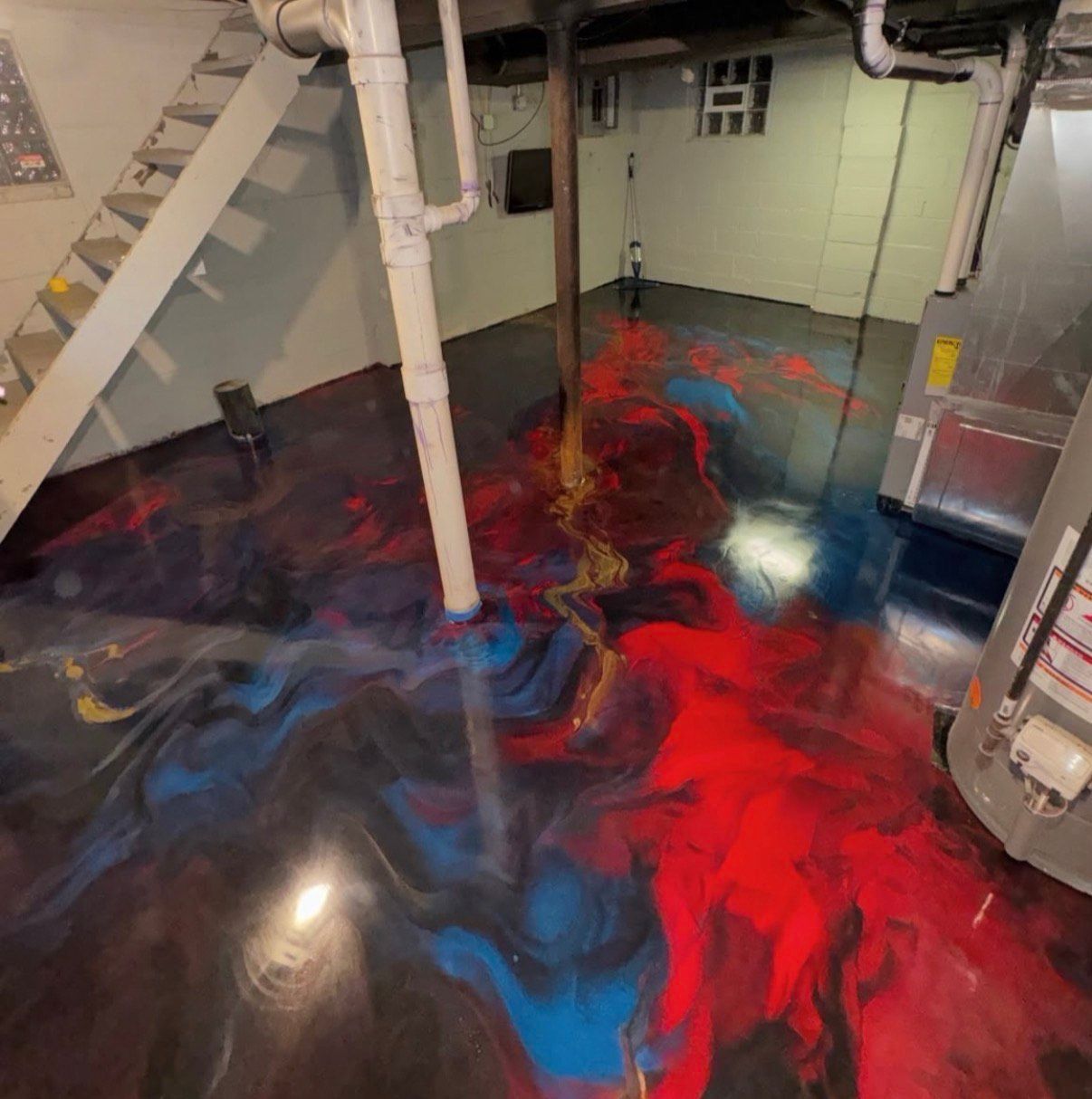 Basement floor with red, blue, and gold epoxy swirl design. Stairs, pipes, and utility equipment are visible.