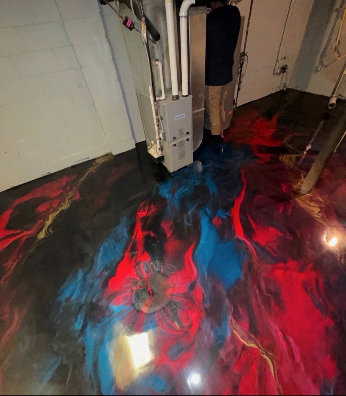 Epoxy floor in red, blue, black, and gold swirls; person standing near a furnace.