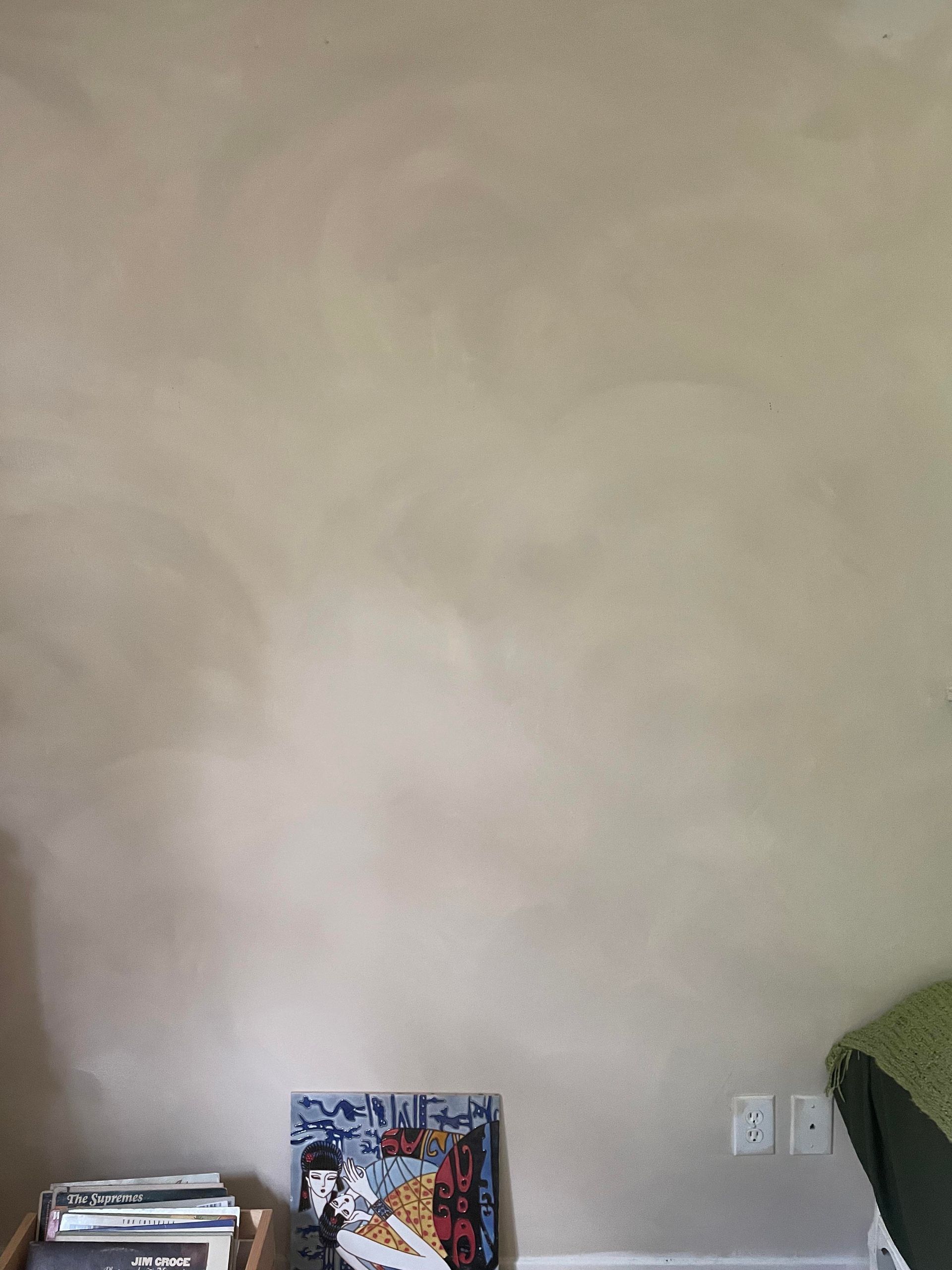 A plain, beige-painted wall with visible brushstroke patterns above a small box of items and a wall outlet.