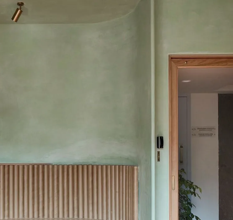 Green-painted wall with curved ceiling and wooden slat bench. Doorway framed in wood.