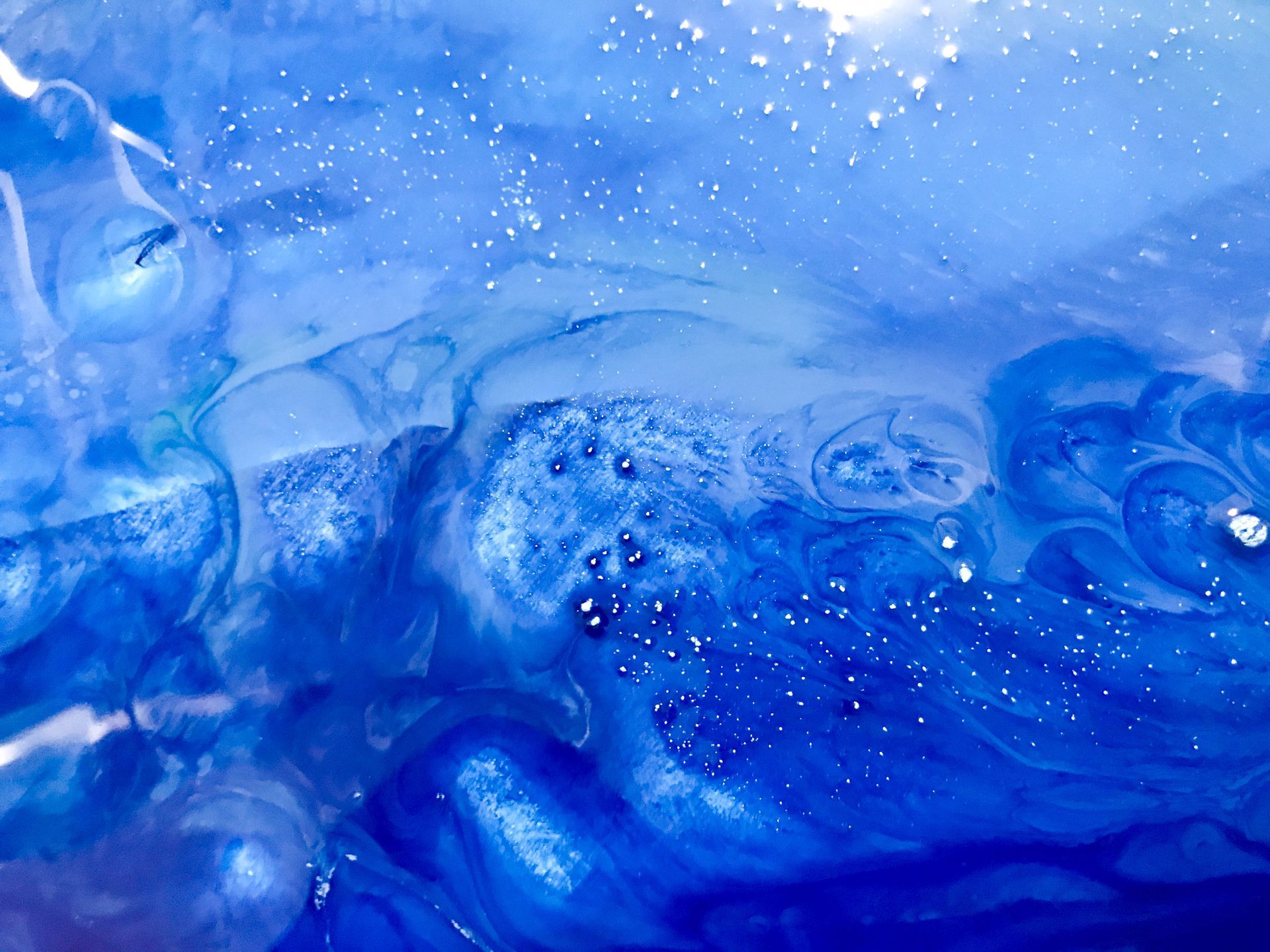 Abstract blue and white art, resembling water with swirls, bubbles, and a few white specks.