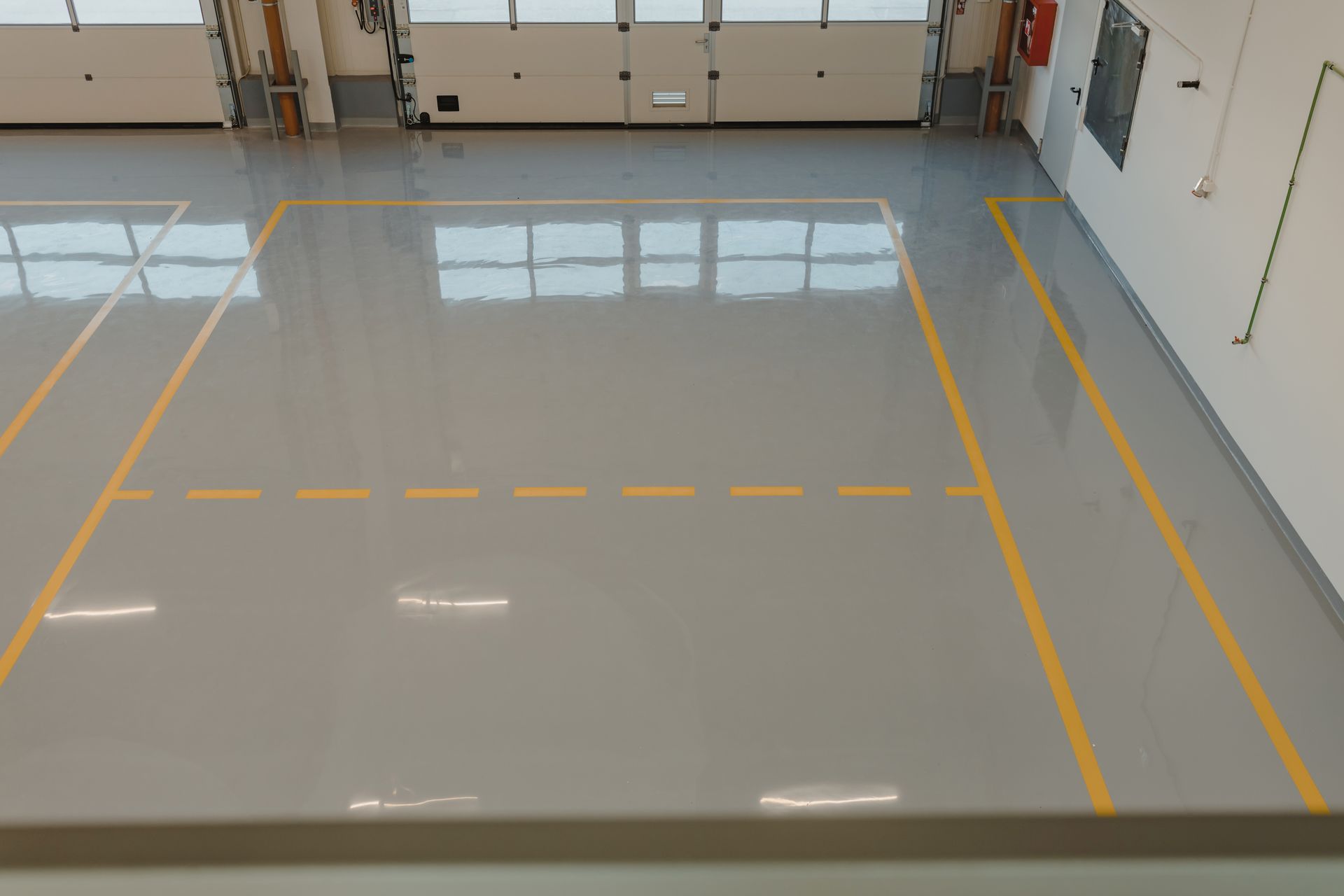 A gray floor with yellow lines in a large open space, possibly a warehouse or garage, with overhead doors visible.