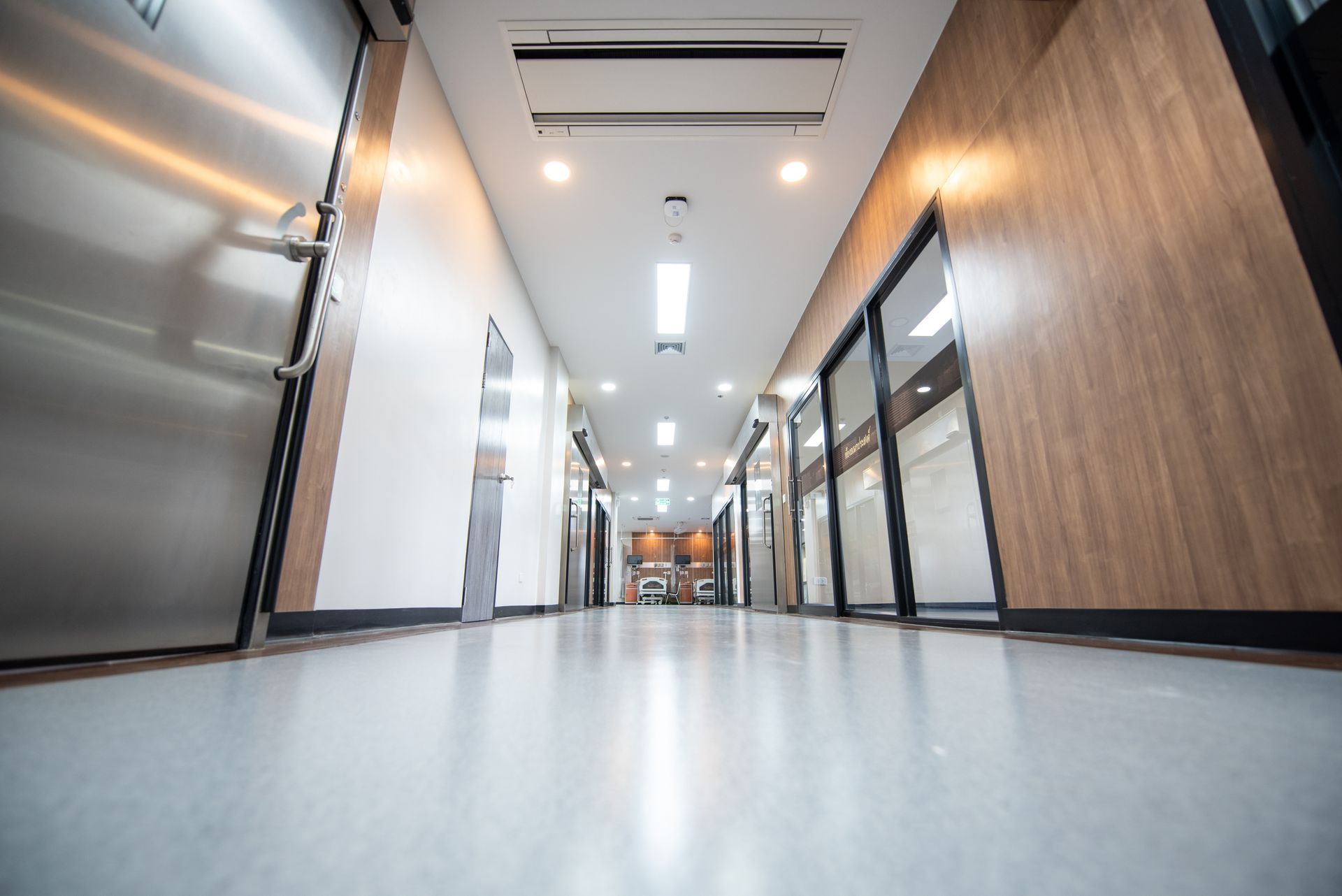 Long hallway with wood-paneled walls, bright lights, and several closed doors. A large metallic door is on the left.