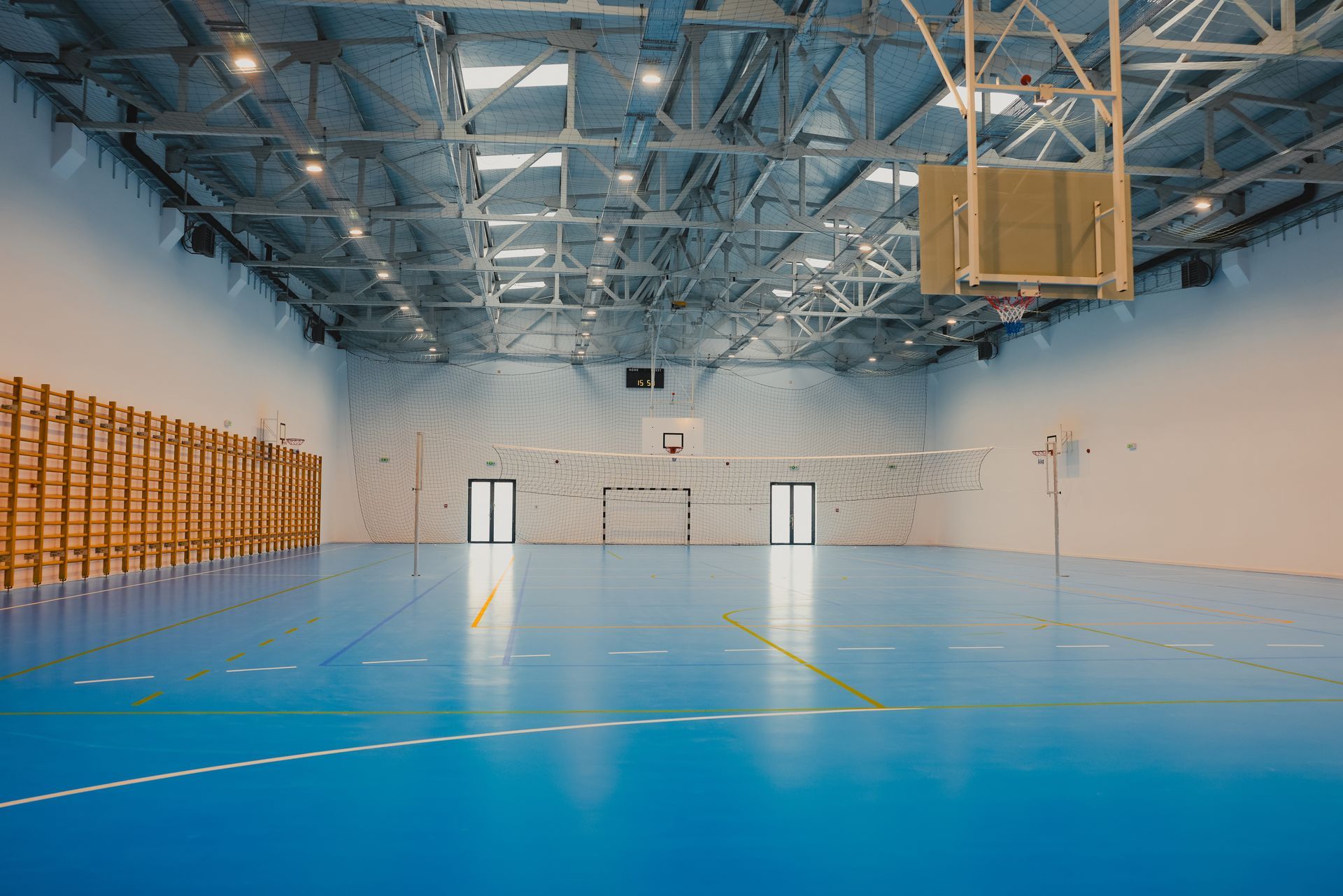 Blue indoor sports court with basketball hoop, lights, and stacked wooden panels.
