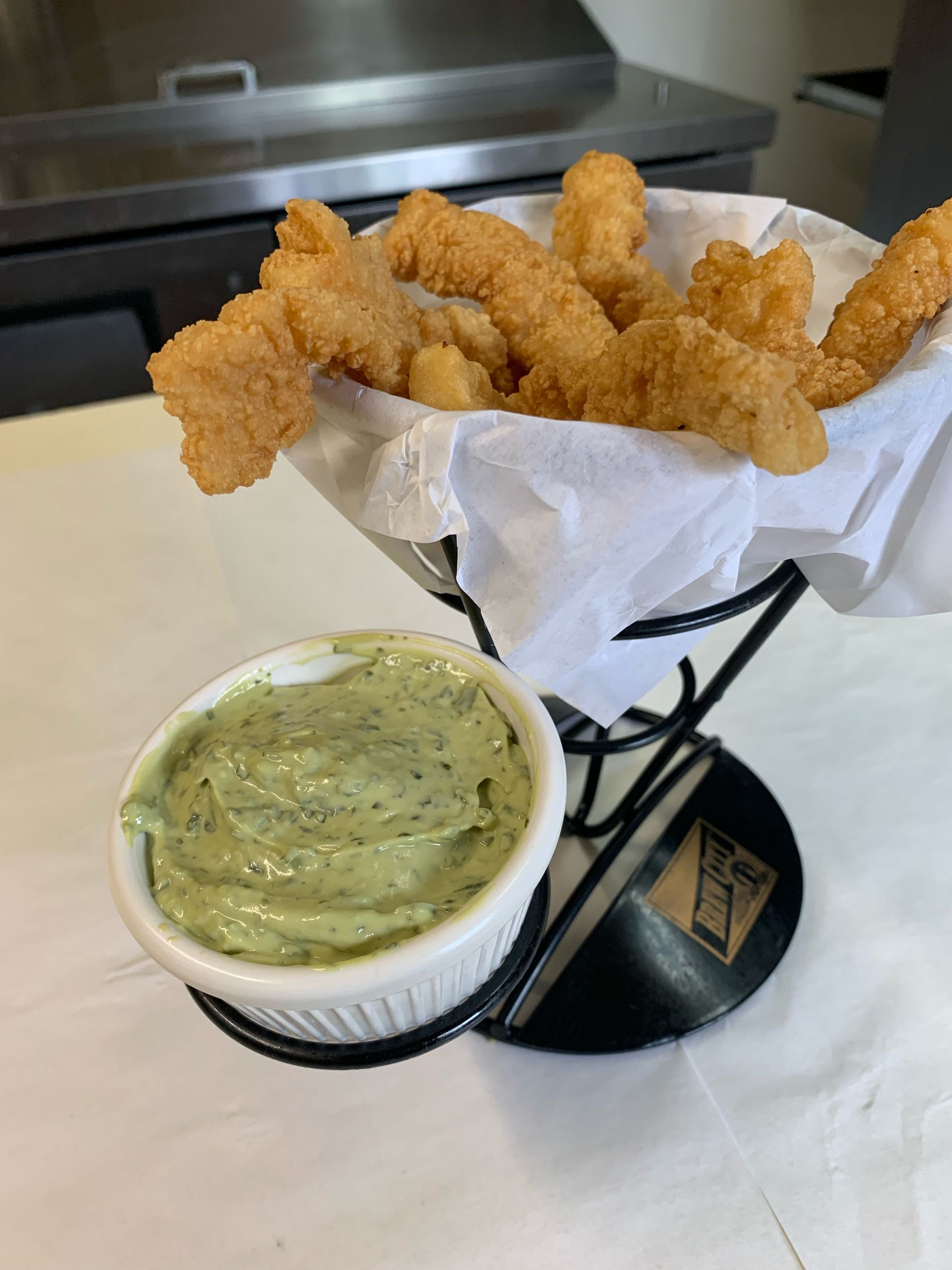 A basket of fried fish and a bowl of guacamole on a table.