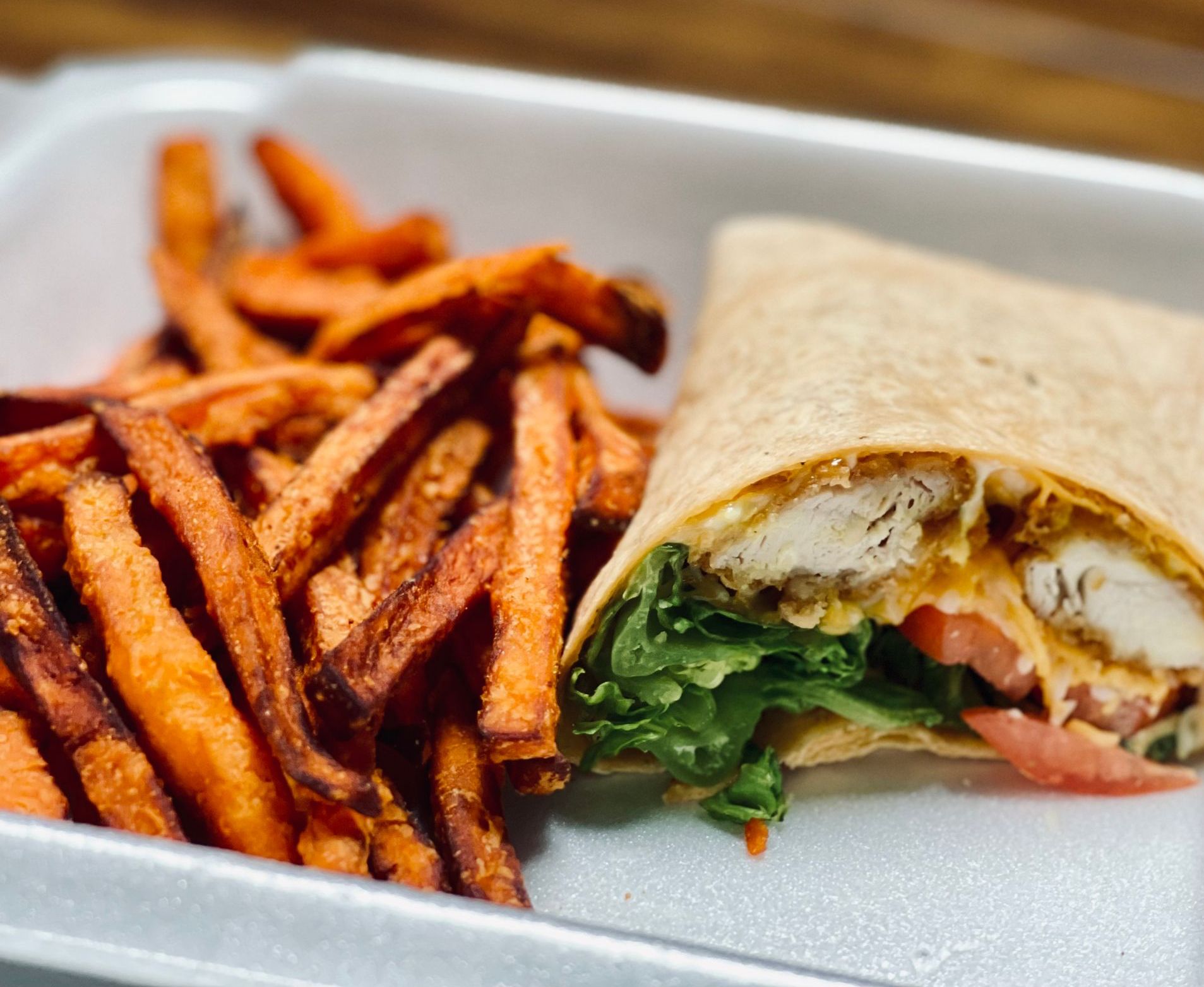 A chicken wrap and sweet potato fries in a styrofoam container