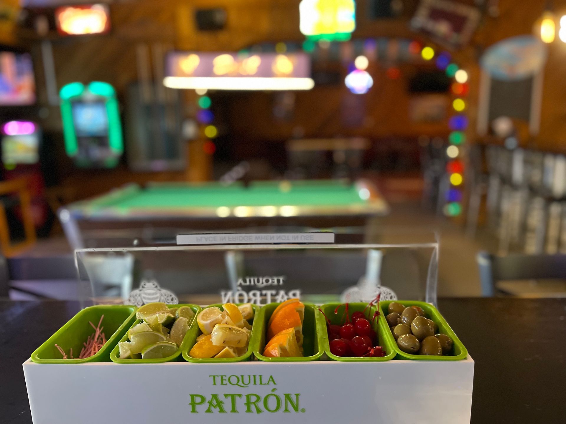 A box of tequila patron sits on a bar next to a pool table.