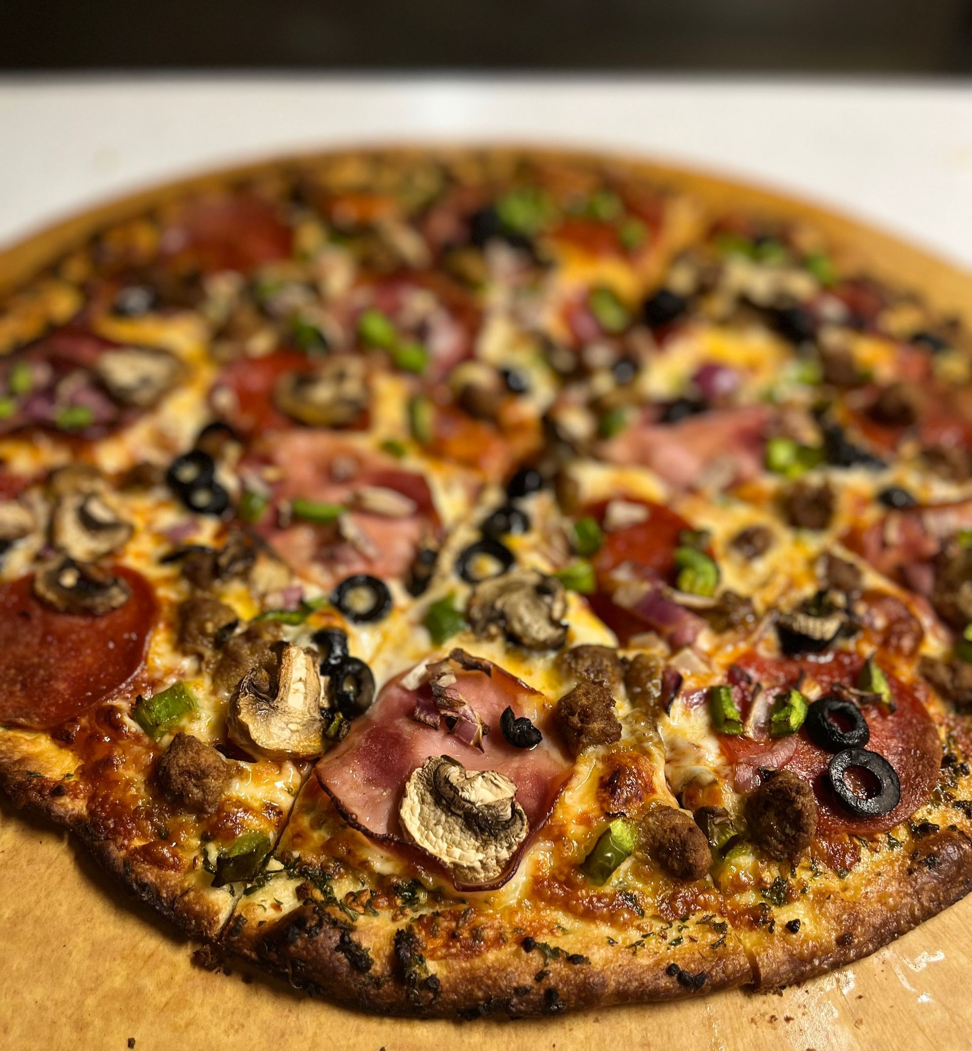 A pizza with a lot of toppings on it is sitting on a wooden table.