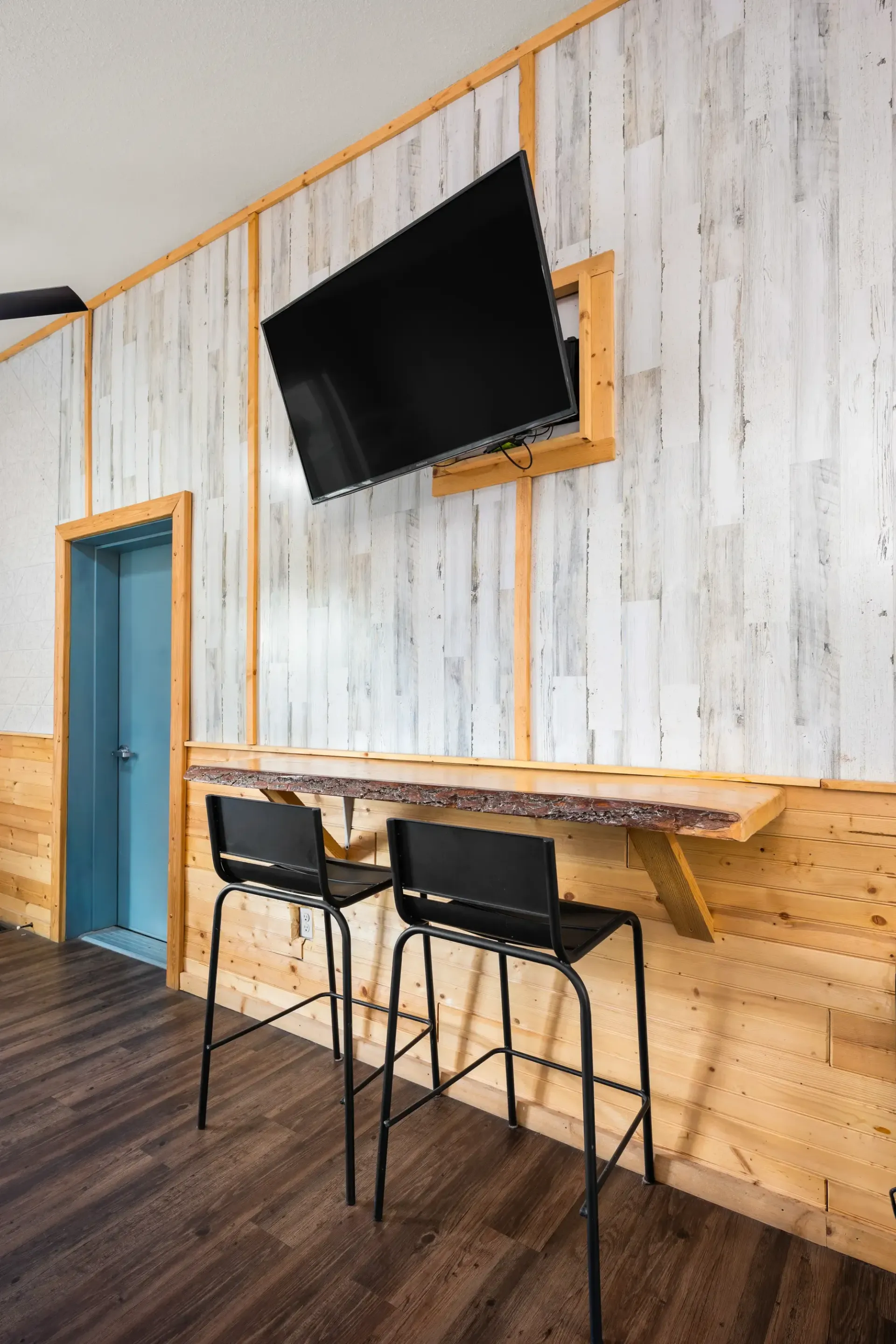 A room with two bar stools and a flat screen tv on the wall.