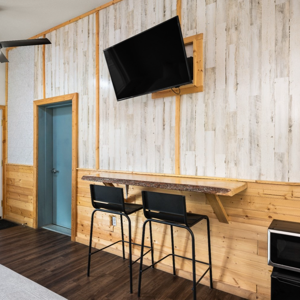 A living room with two bar stools and a flat screen tv on the wall.