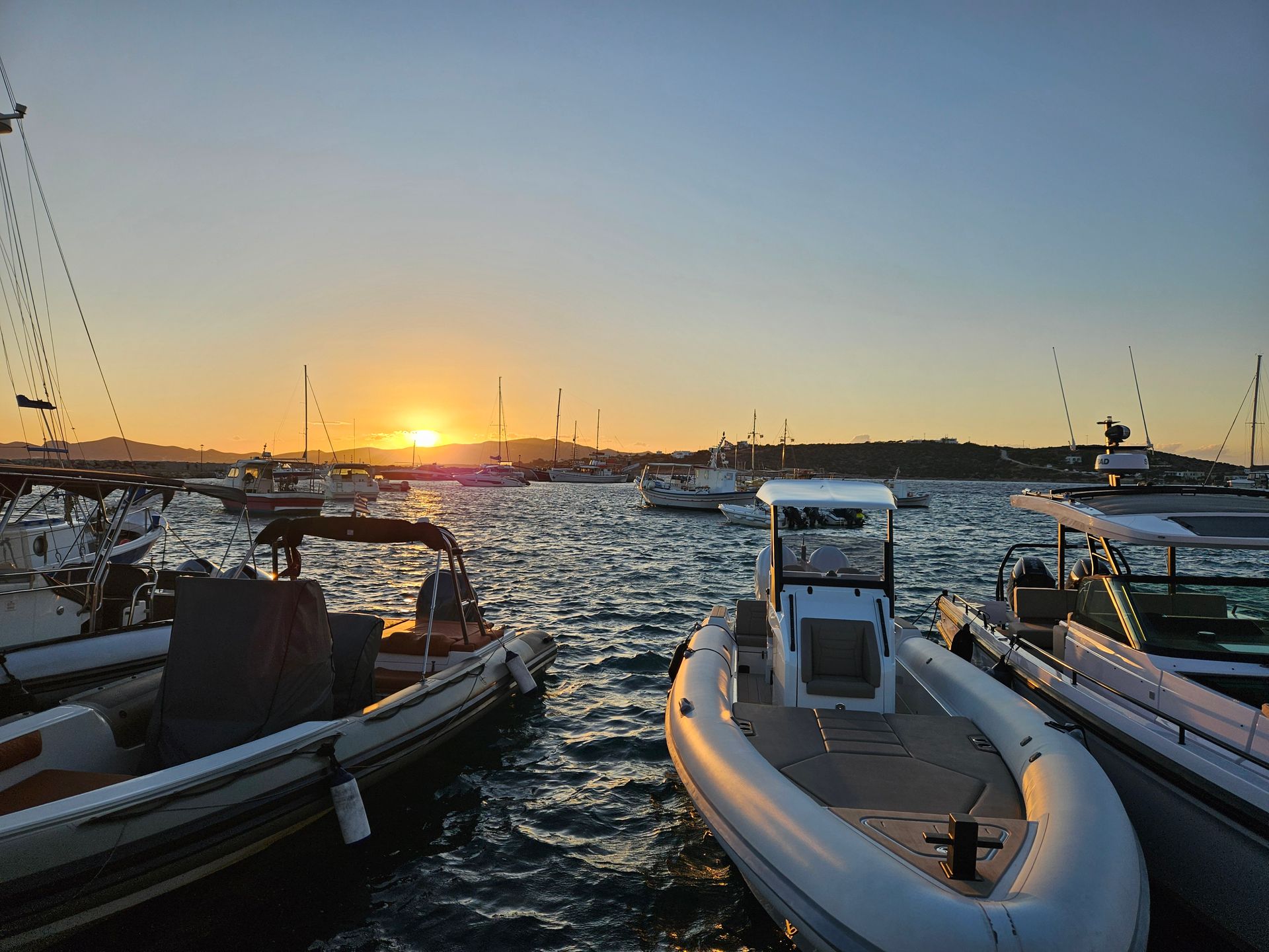 Boats docked in a harbor at sunset. Orange and yellow sky reflects on the water.