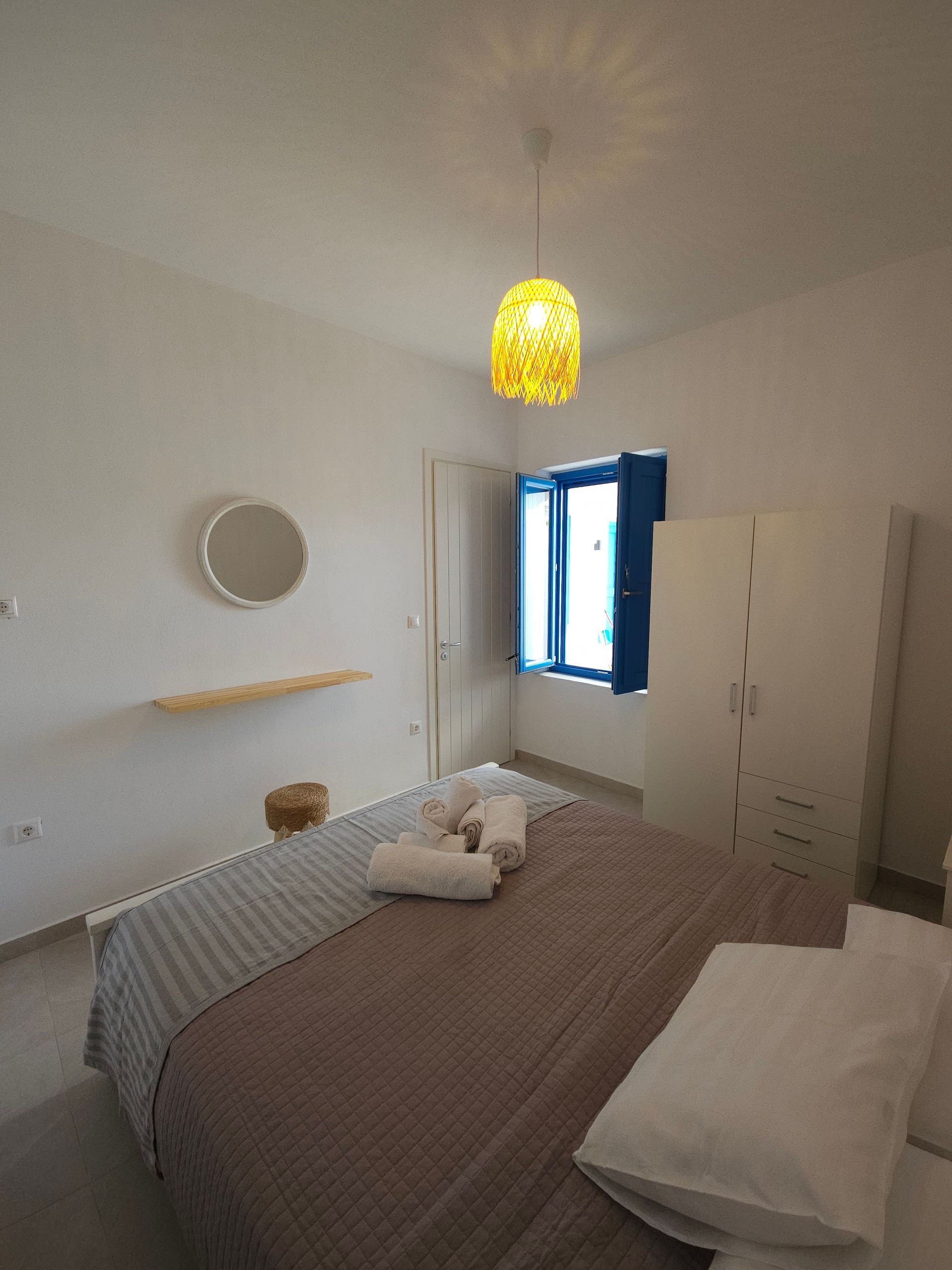 Bedroom with a bed, white walls, blue window, and woven yellow light fixture.