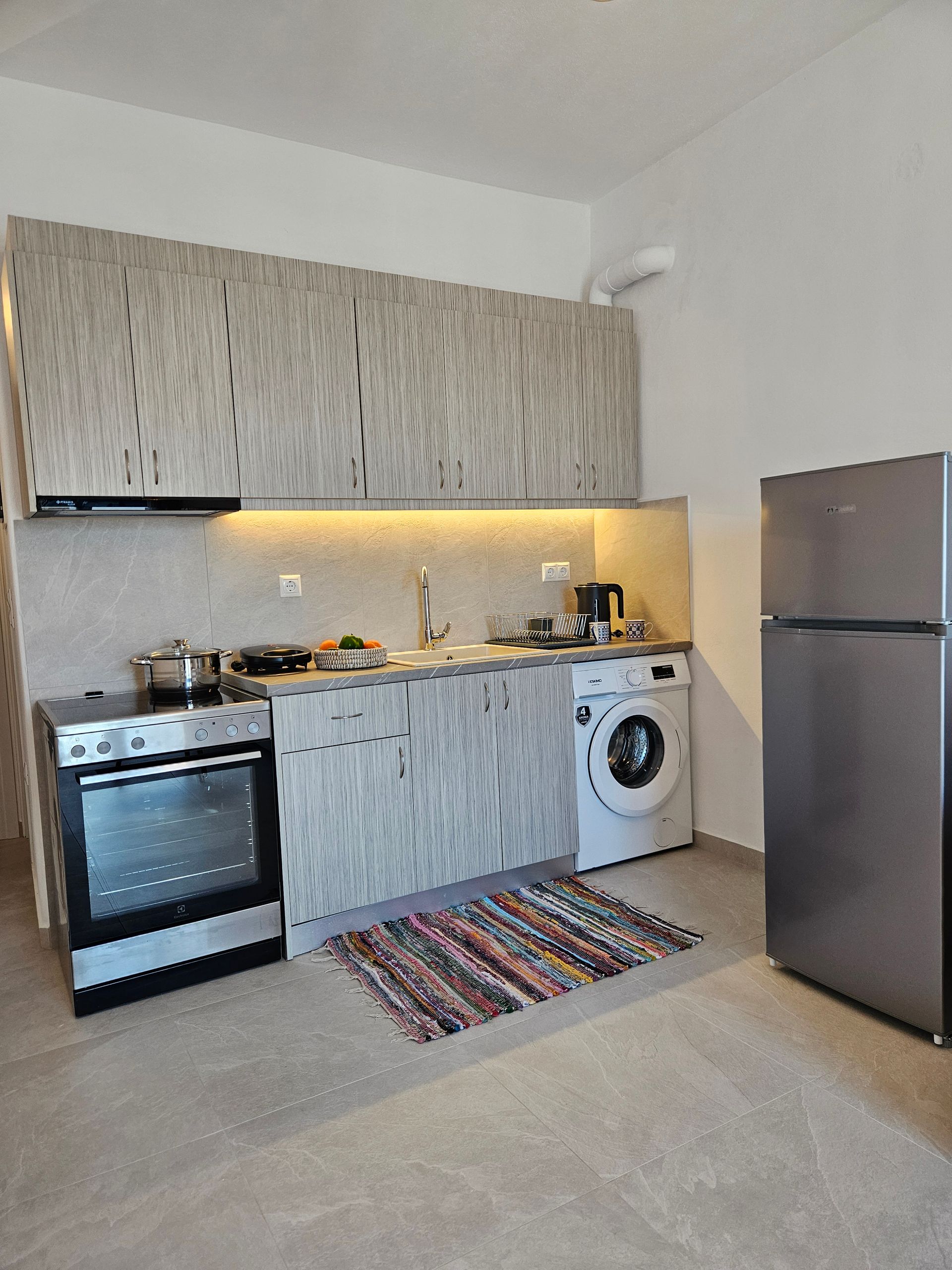 Small kitchen with a stainless steel stove, washing machine, and refrigerator. Light gray cabinets and counter.
