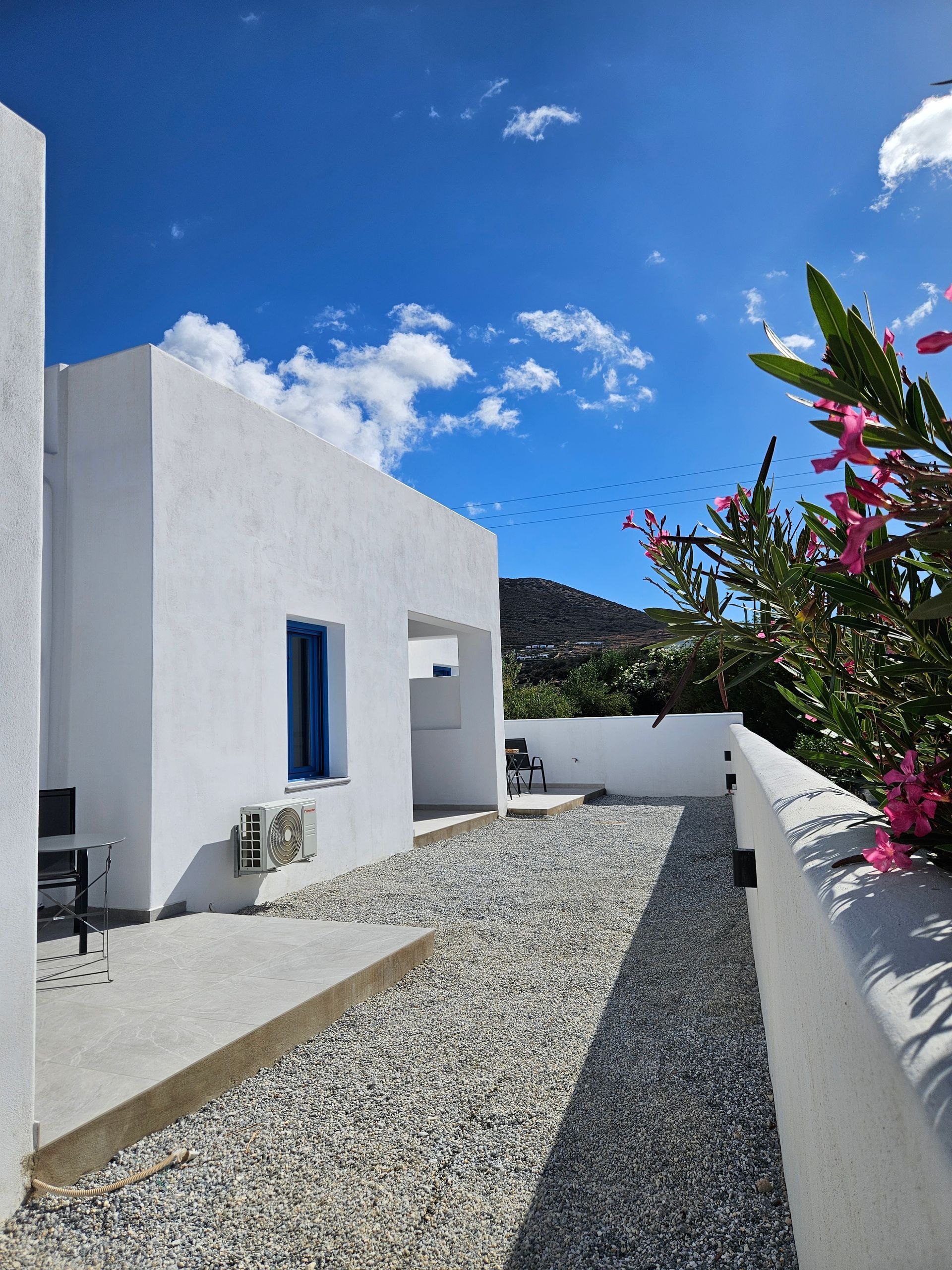 White building with blue sky, gravel path, and pink flowers.