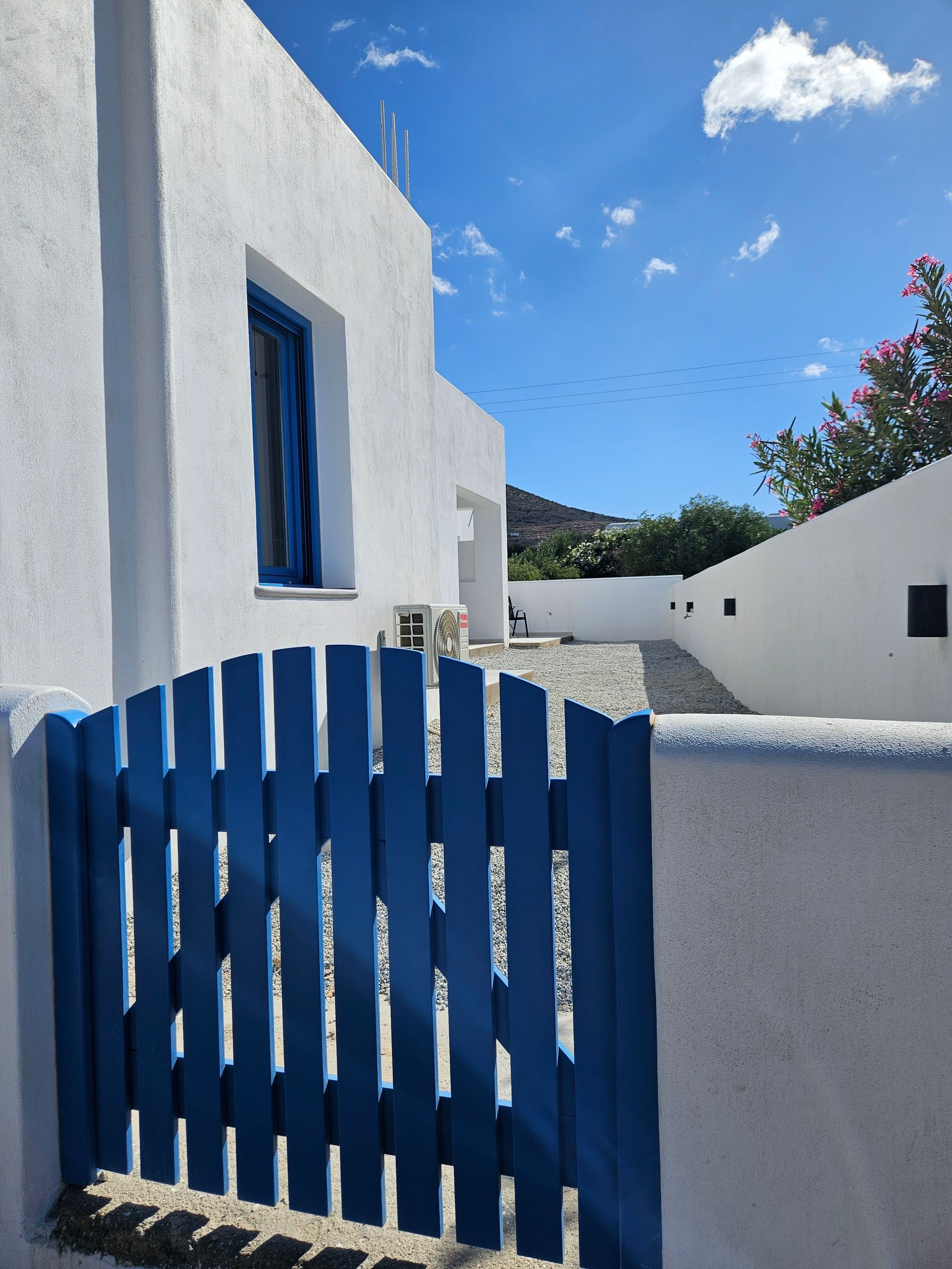 Blue gate in front of a white building with blue window frames, sunny sky.