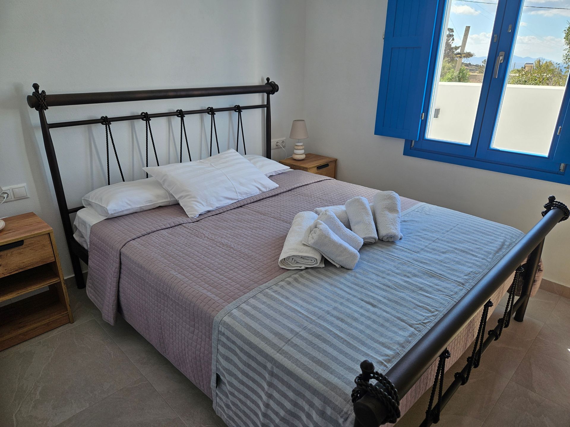 Bedroom with a wrought-iron bed frame, white bedding, and blue window shutters.