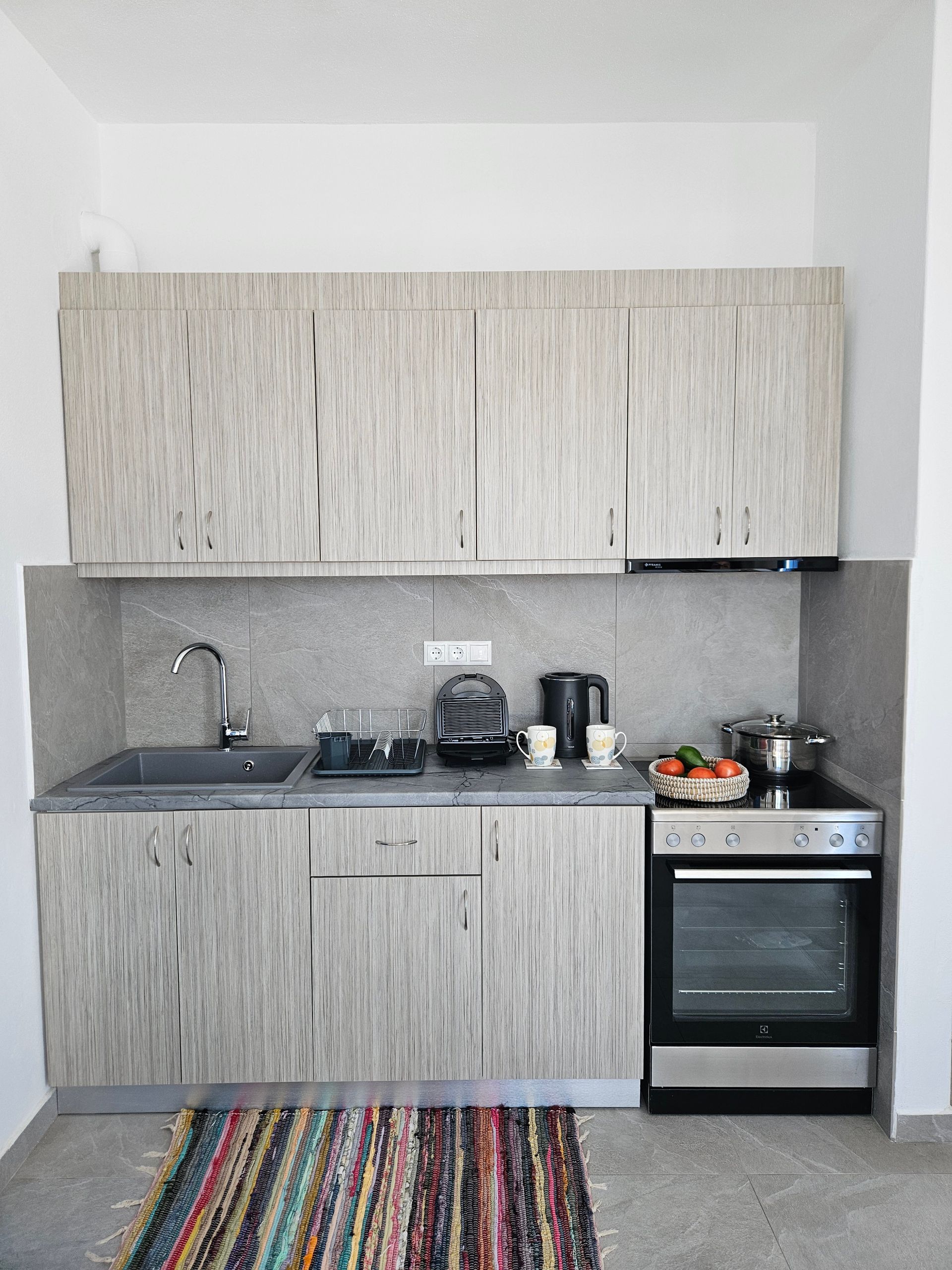 Small kitchen with light wood-grain cabinets, stainless steel appliances, and a colorful rug.