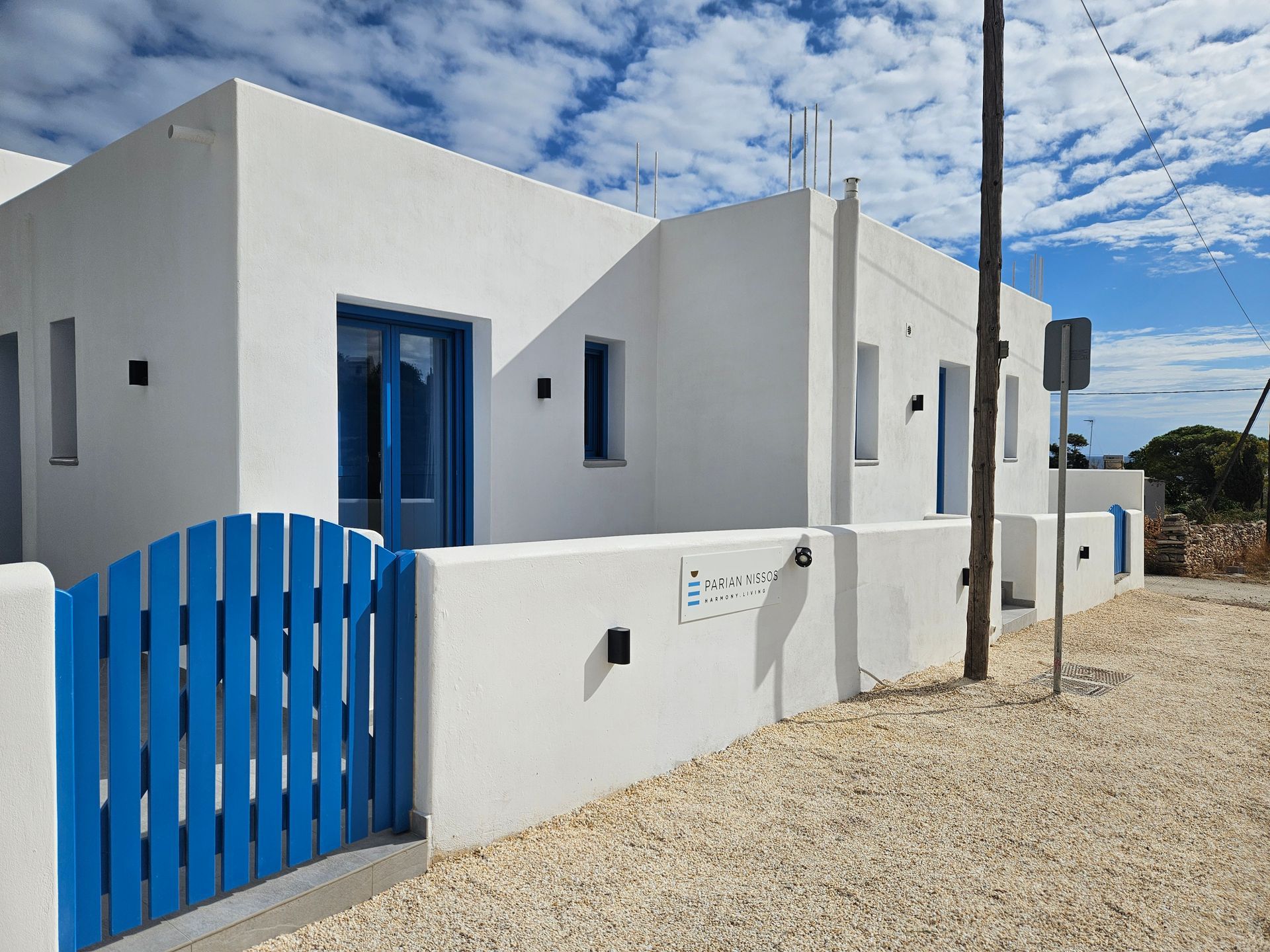 White building with blue accents, gate, and door under a cloudy sky.