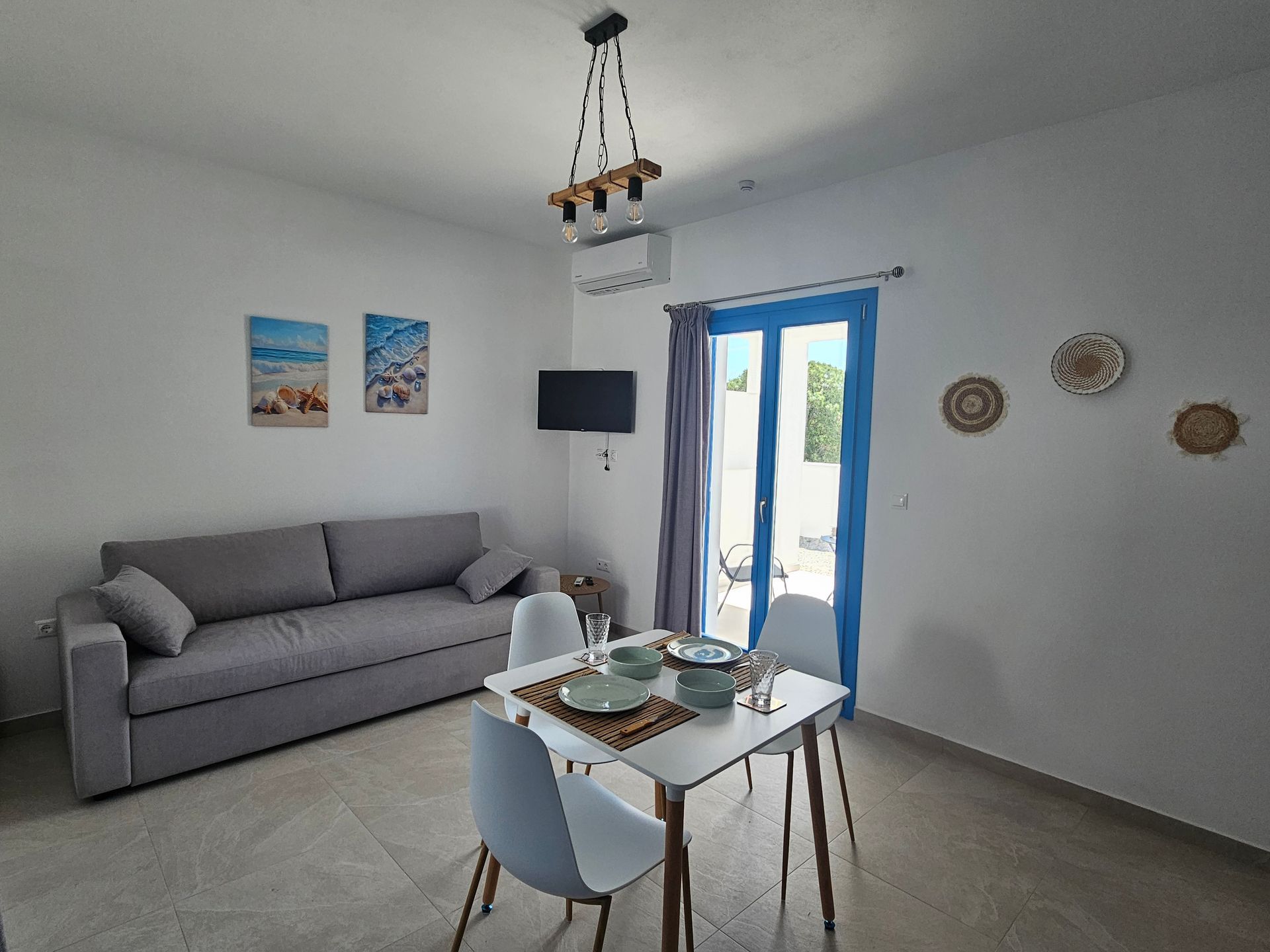 A modern, bright living space with a grey sofa, small table, dining table and chairs, and a blue-framed door.
