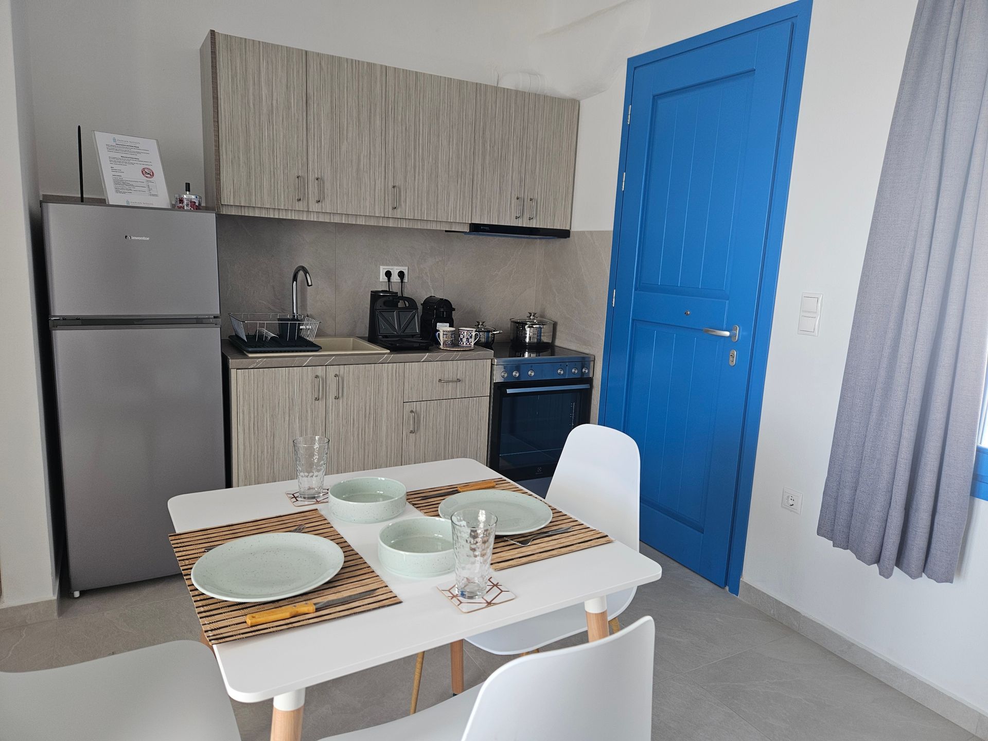 Small studio kitchen and dining area with white walls, blue door, and simple furniture.