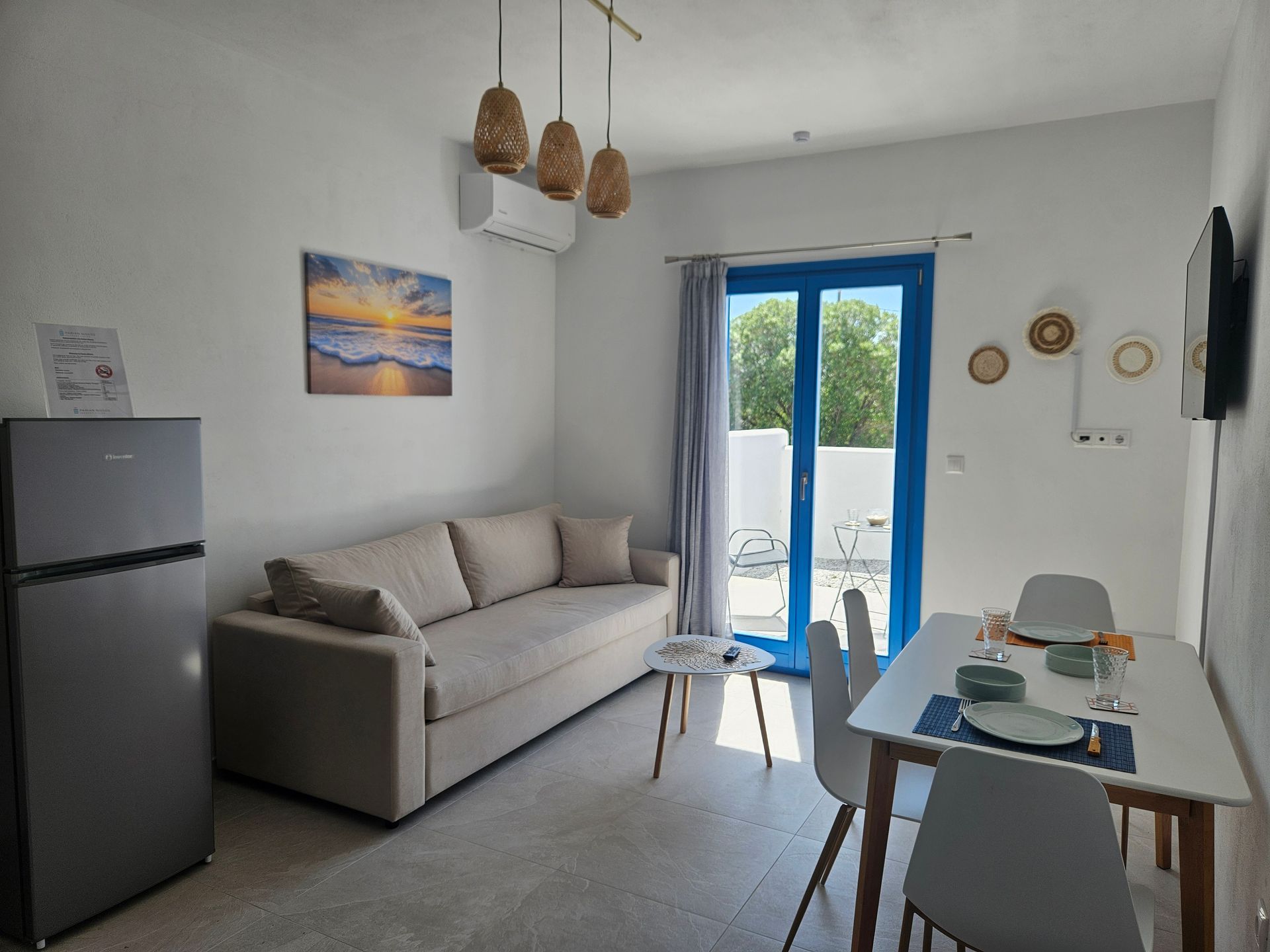 Living room with cream sofa, white walls, blue door to a small patio, and hanging amber lights.