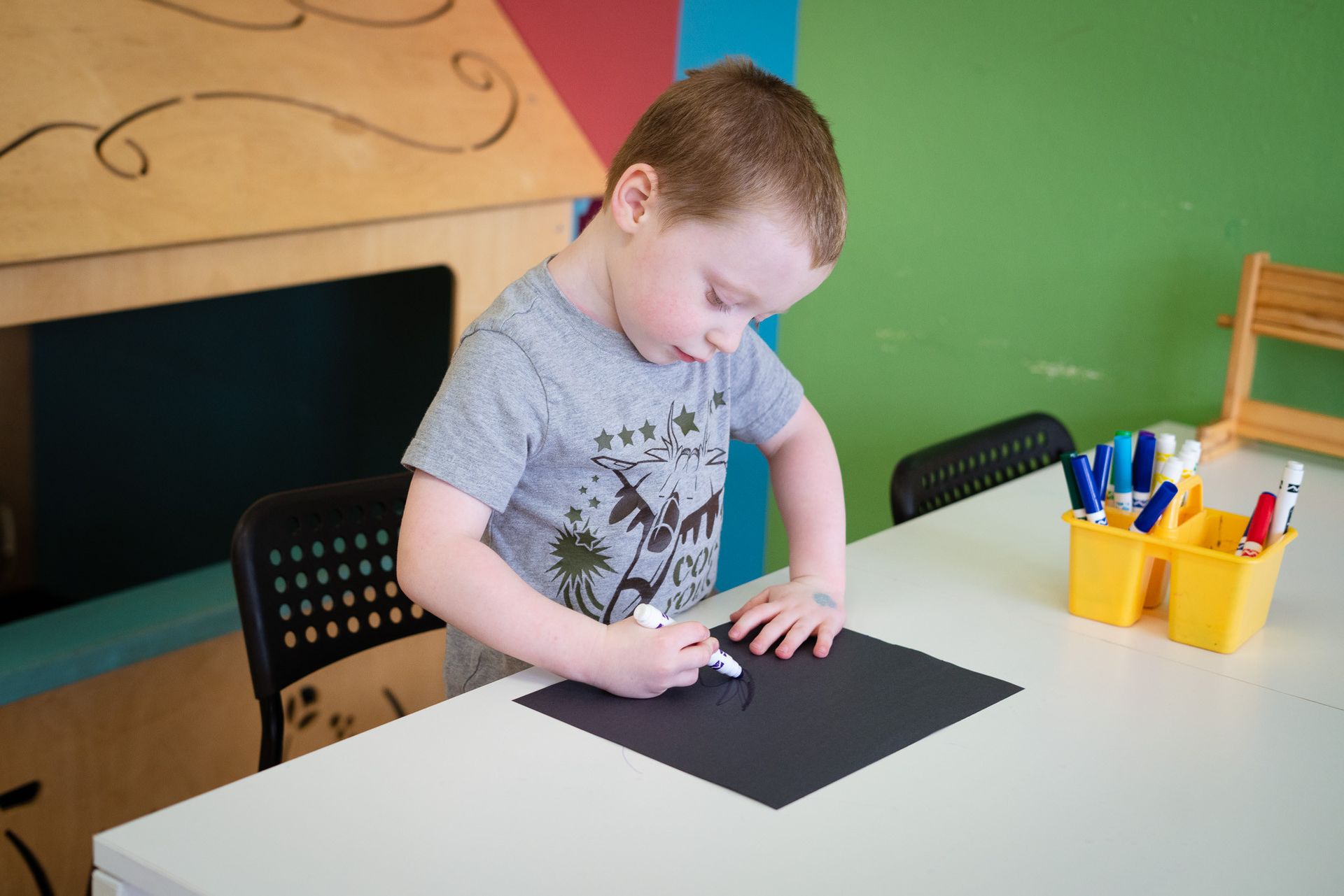 A young boy is sitting at a table drawing on a piece of paper.