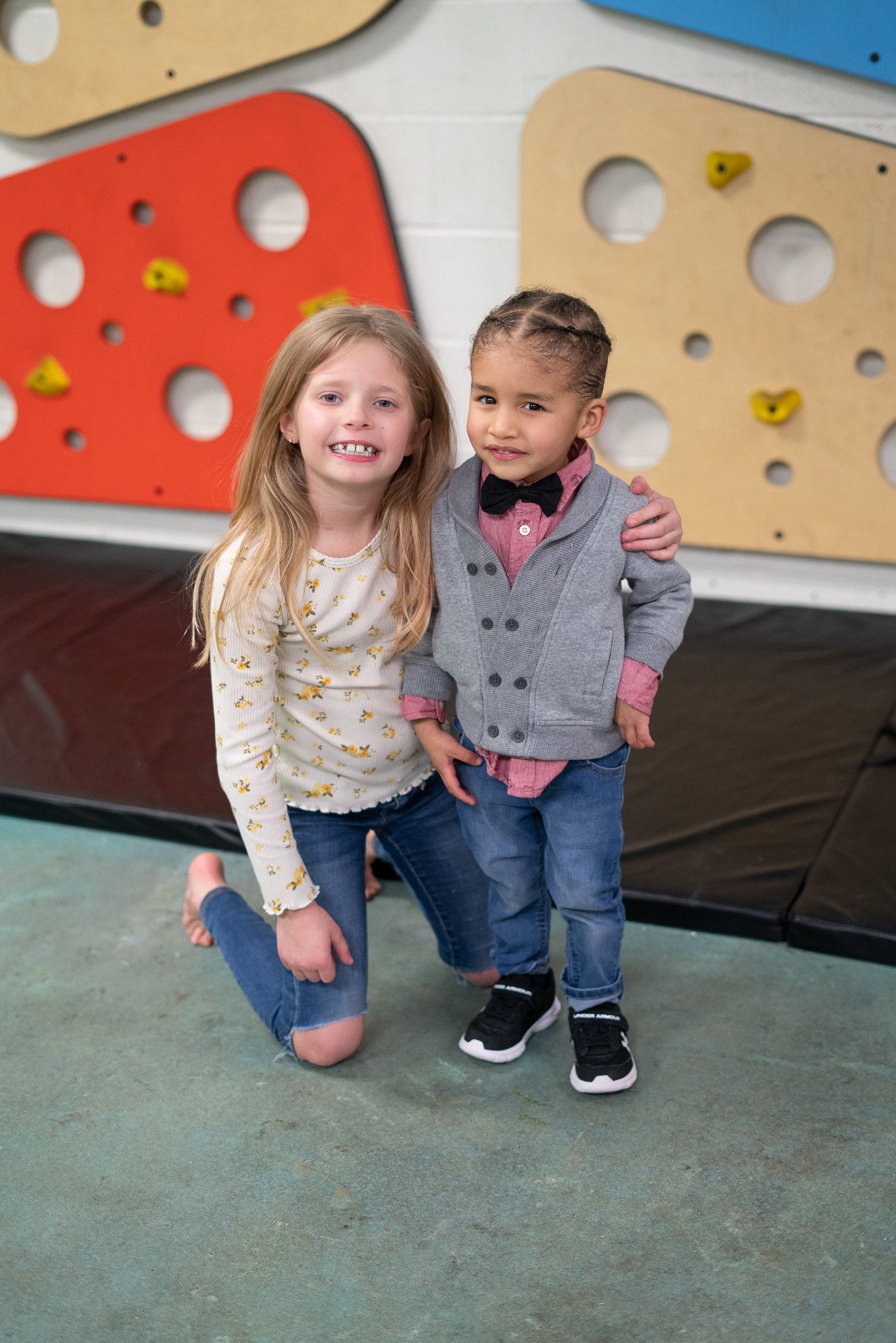 A boy and a girl are posing for a picture in front of a cheese wall.