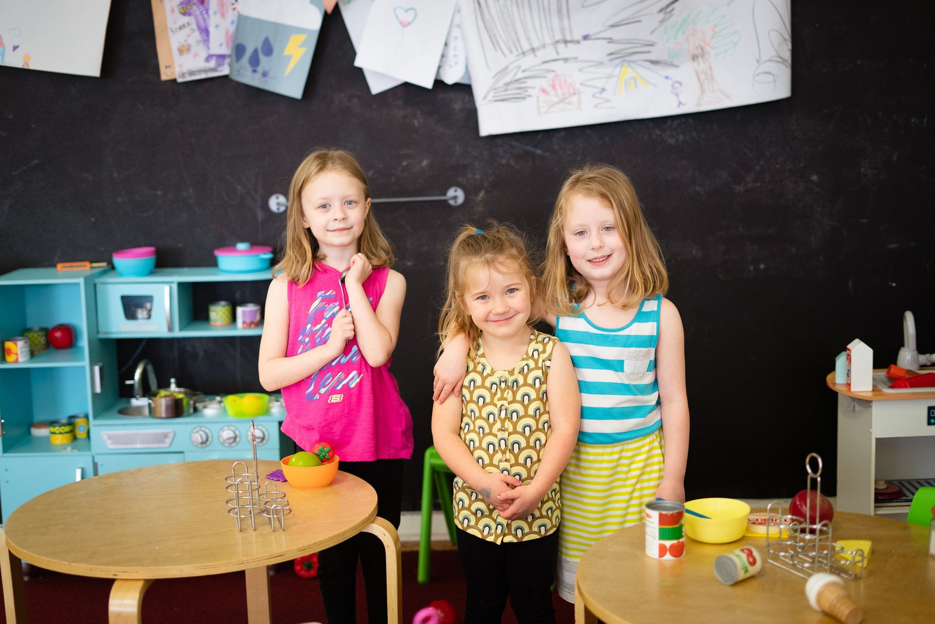 Three little girls are posing for a picture in a play room.