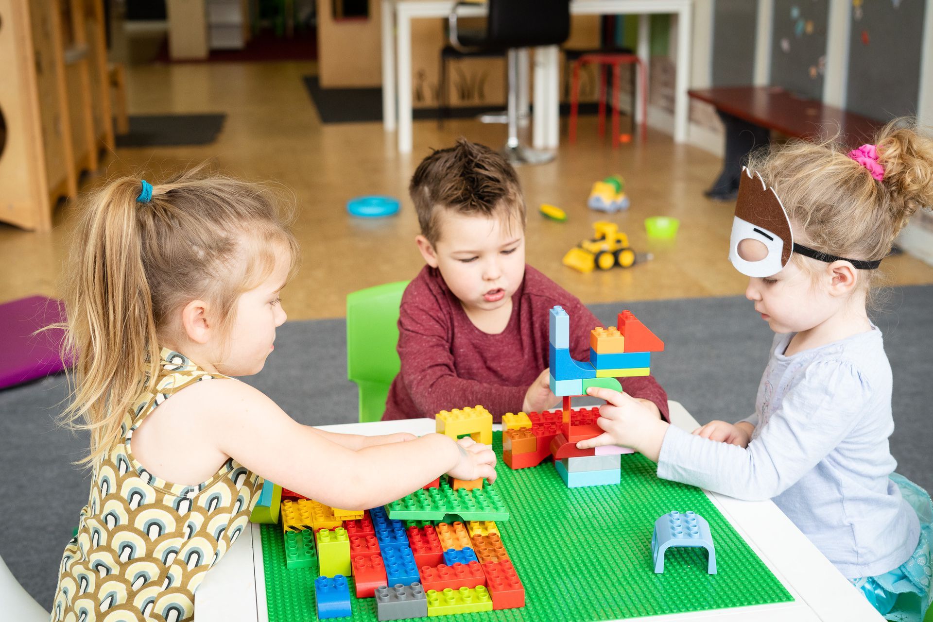 Three children are playing with lego blocks at a table.