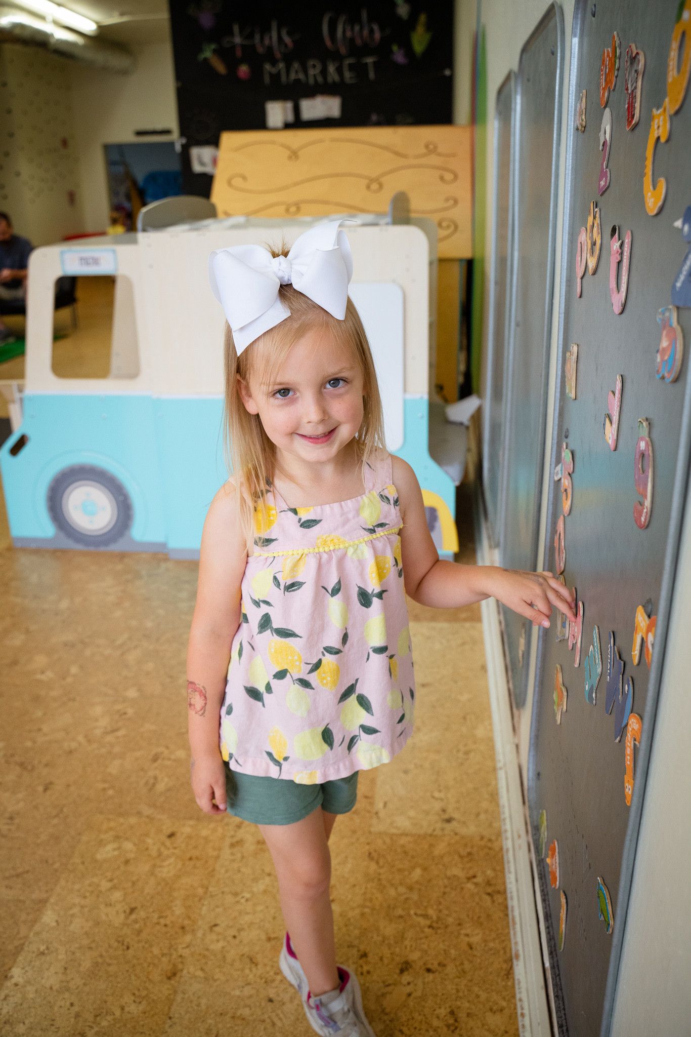 A little girl is standing in front of a bulletin board in a room.