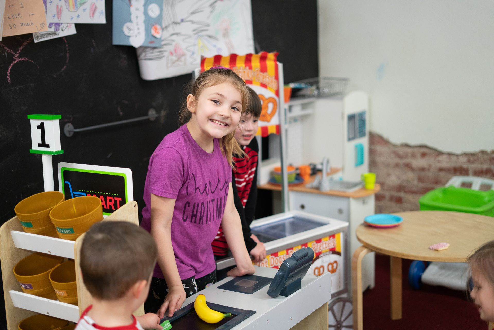 A girl in a purple shirt is standing in front of a play kitchen.