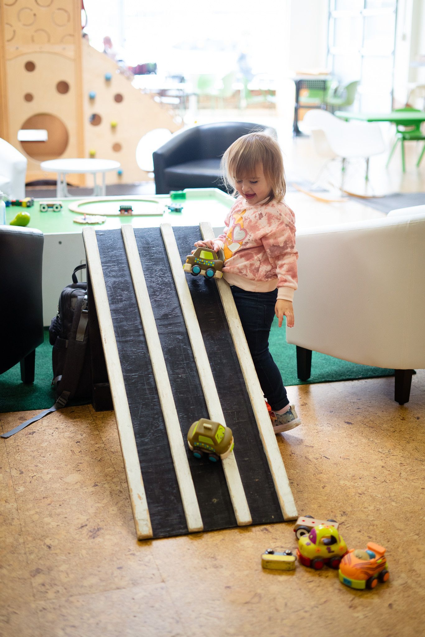 A little girl is playing with a toy car on a ramp.