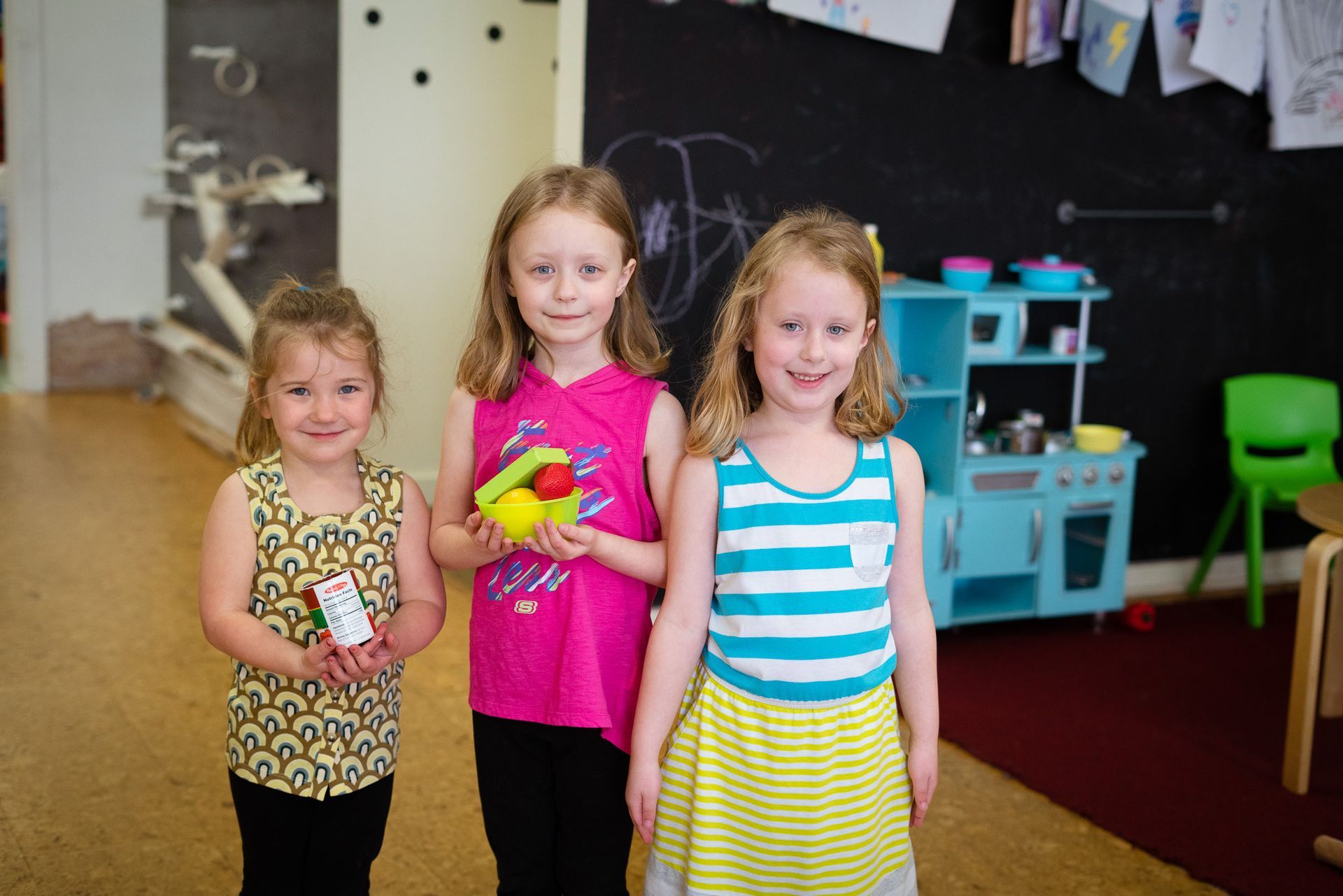 Three little girls are standing next to each other in a room.