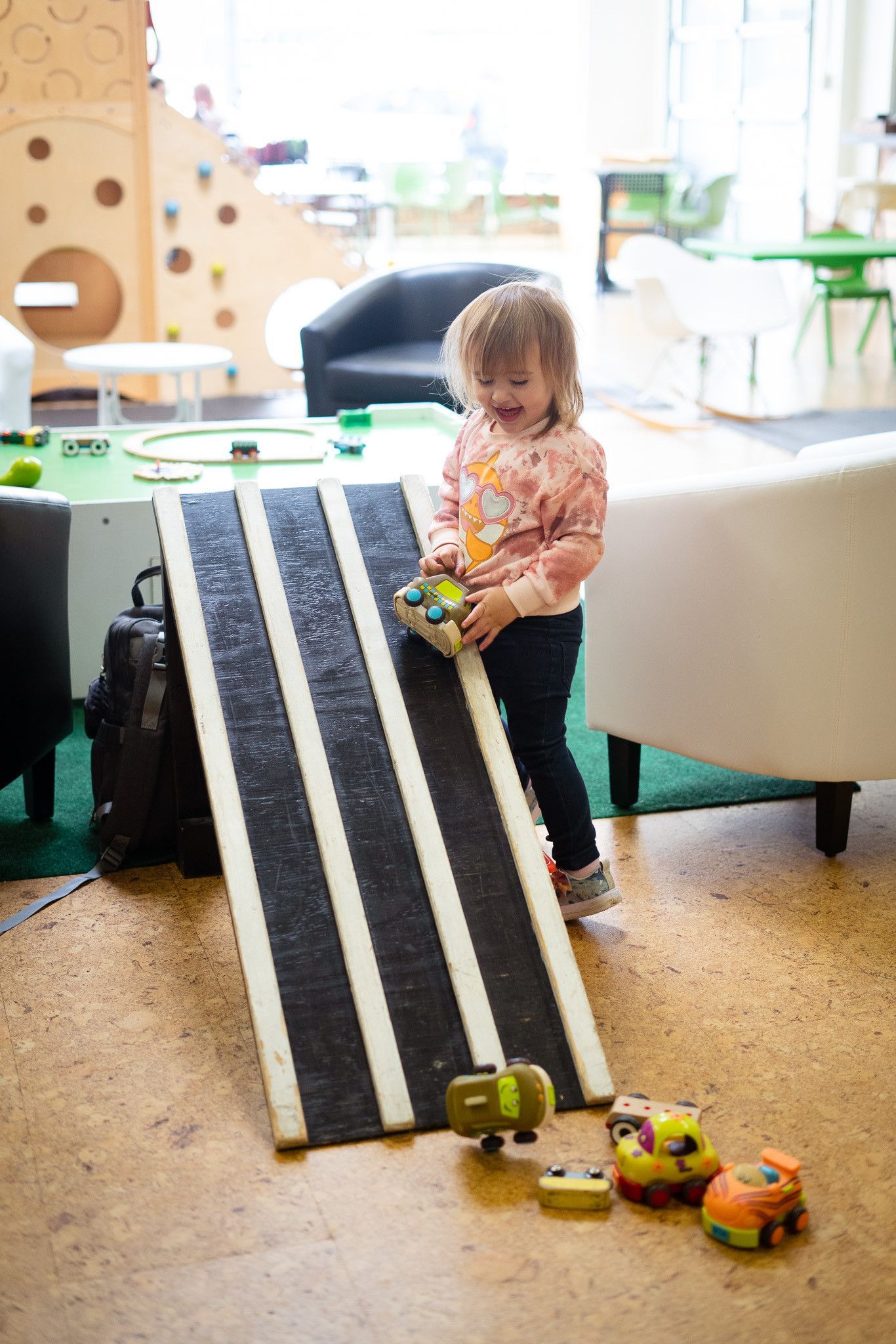 A little girl is playing with toys on a ramp.