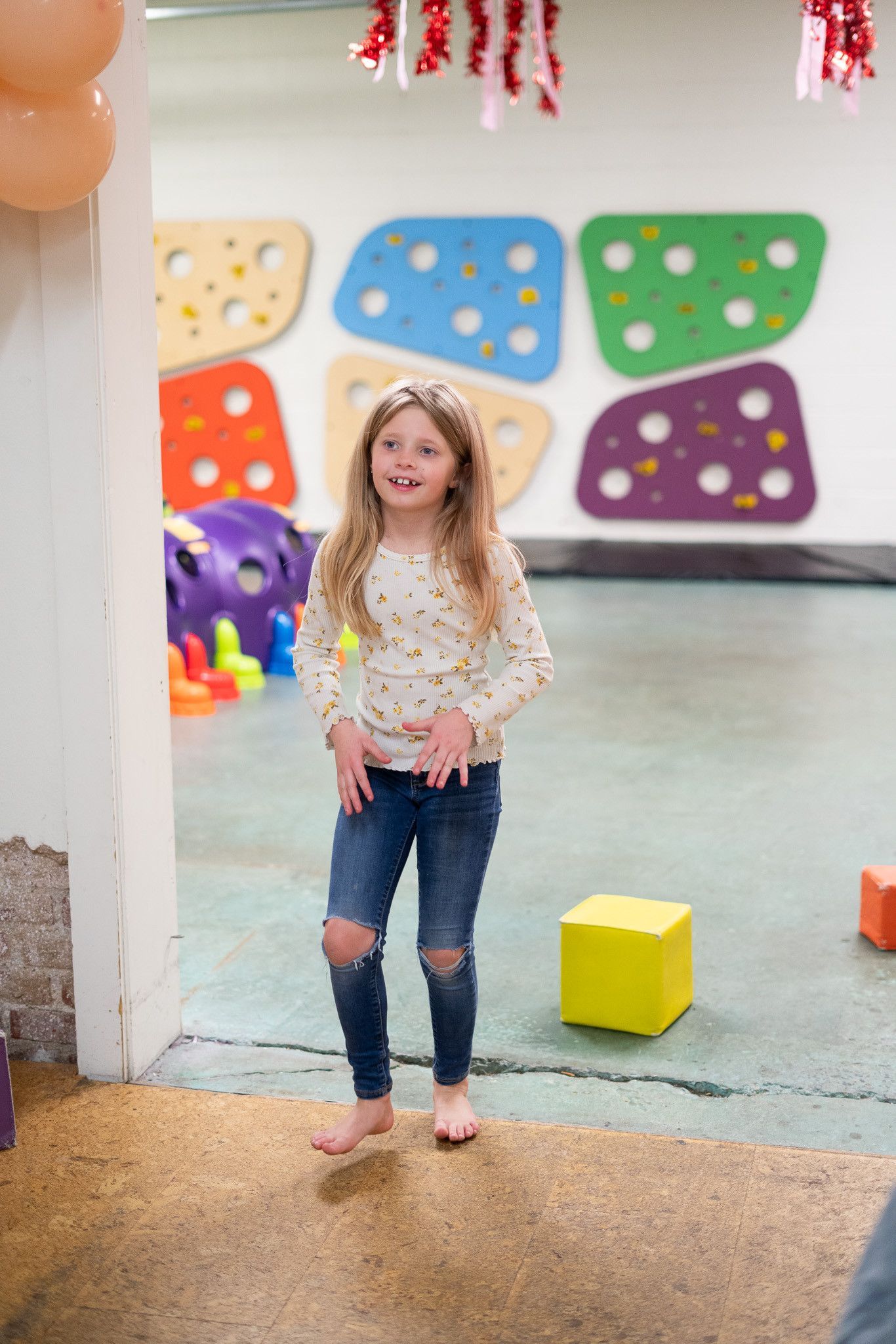 A little girl is standing in a room with balloons on the wall.