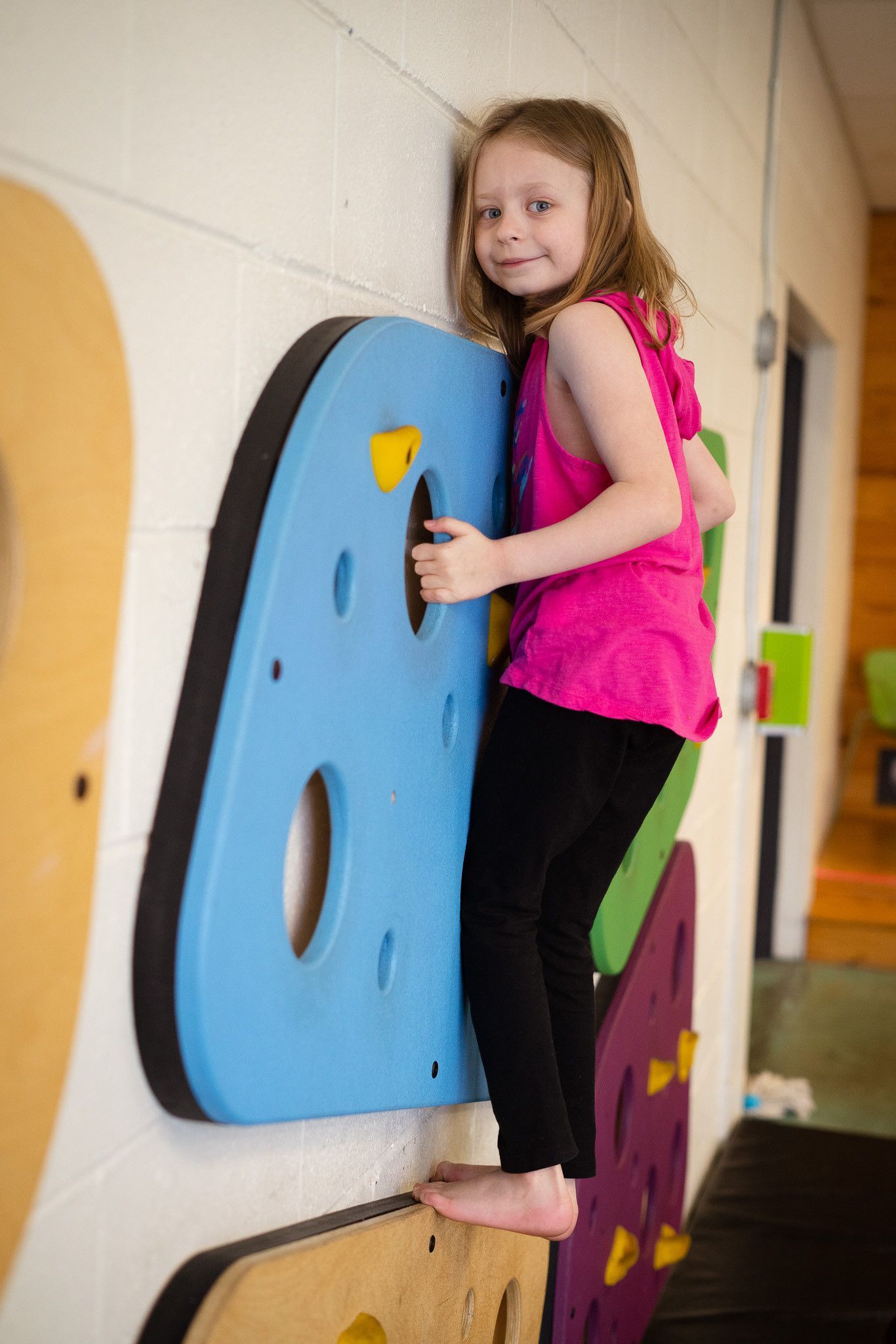 A little girl in a pink shirt is climbing on a wall.