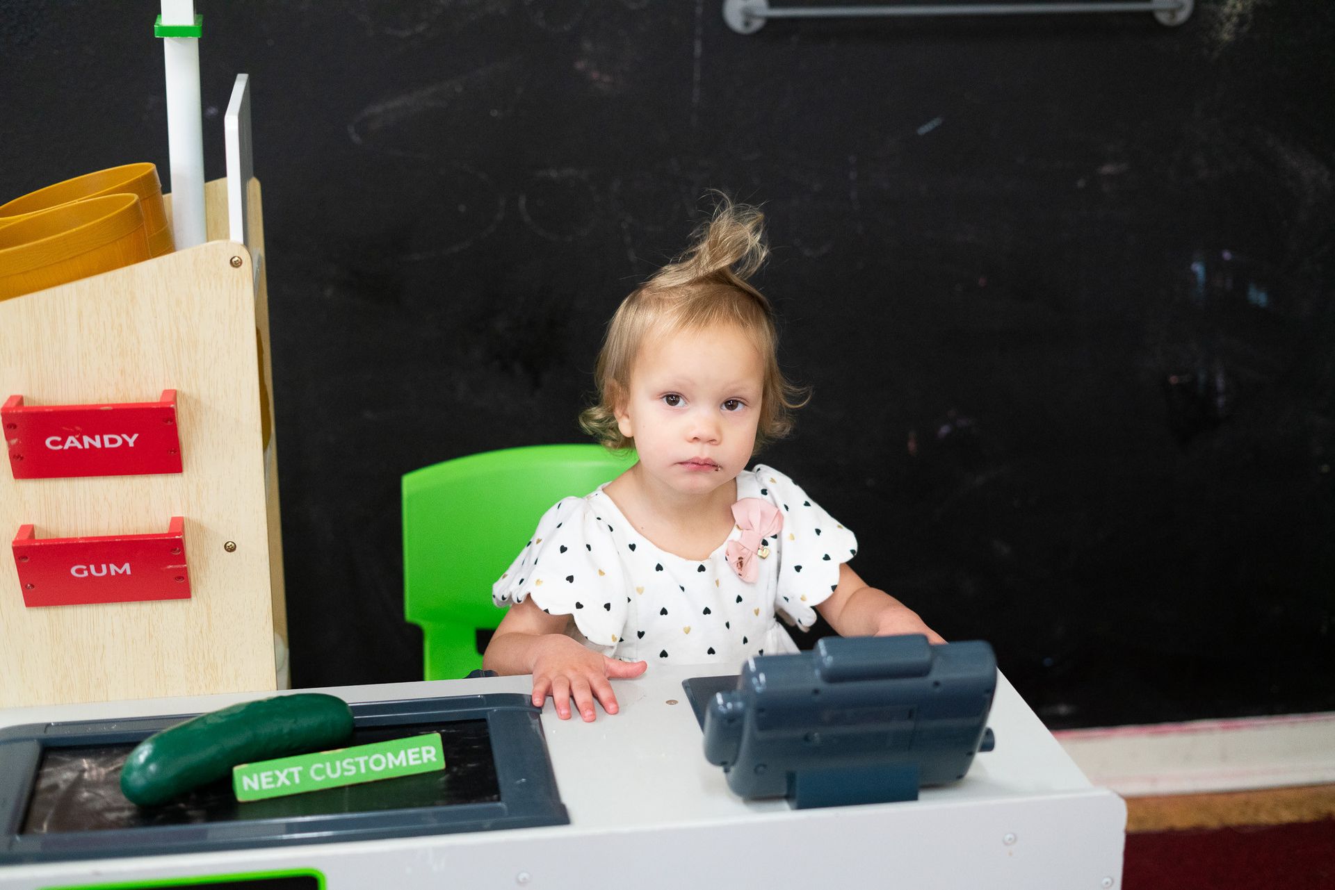 A little girl is sitting at a toy cash register.