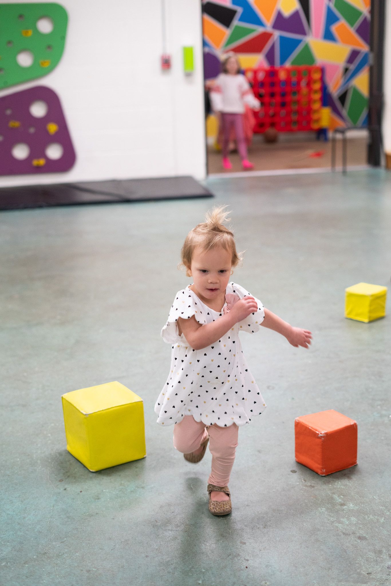 A little girl is running through a room with blocks on the floor.