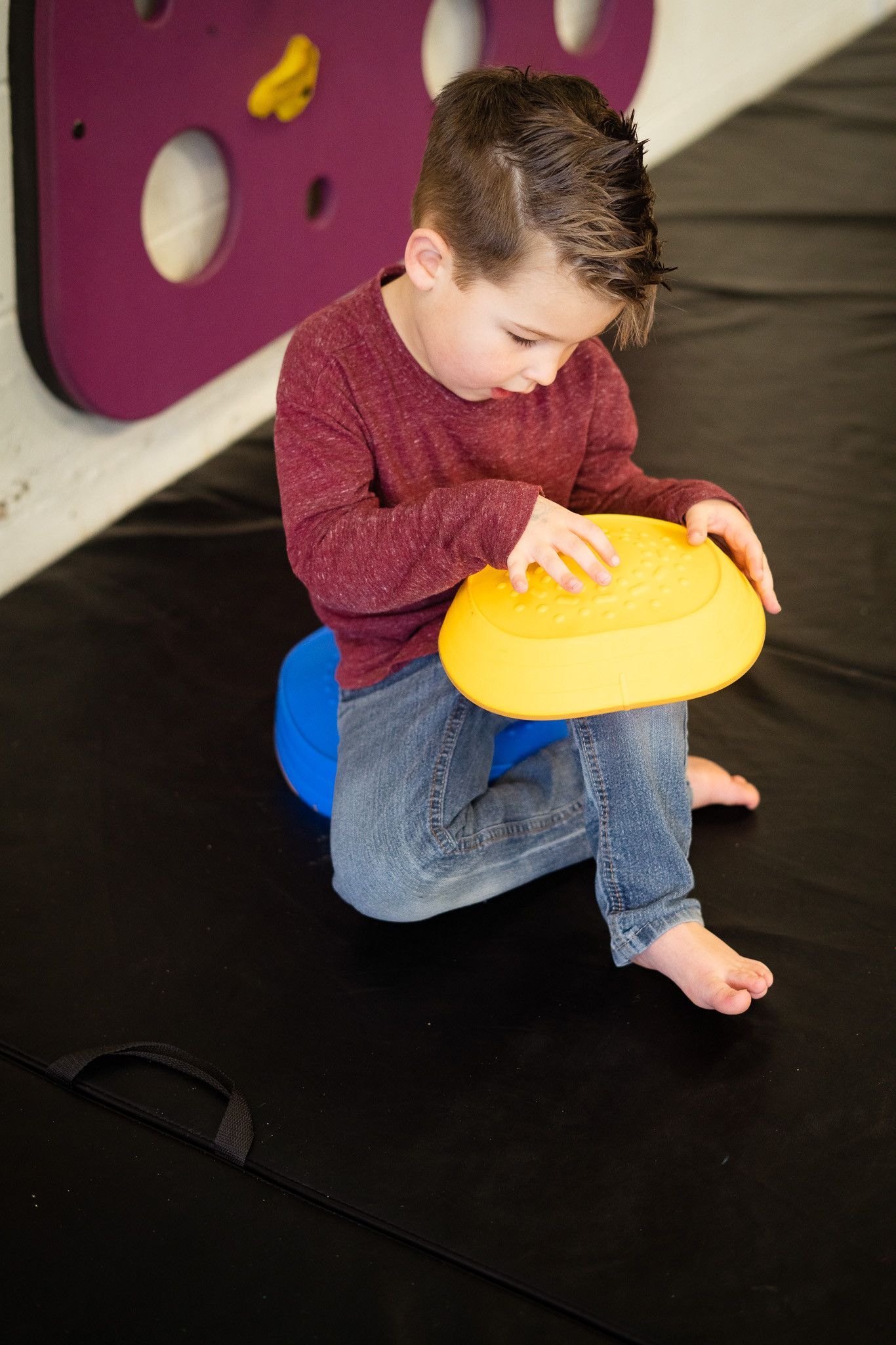 A young boy is sitting on the floor playing with a yellow ball.