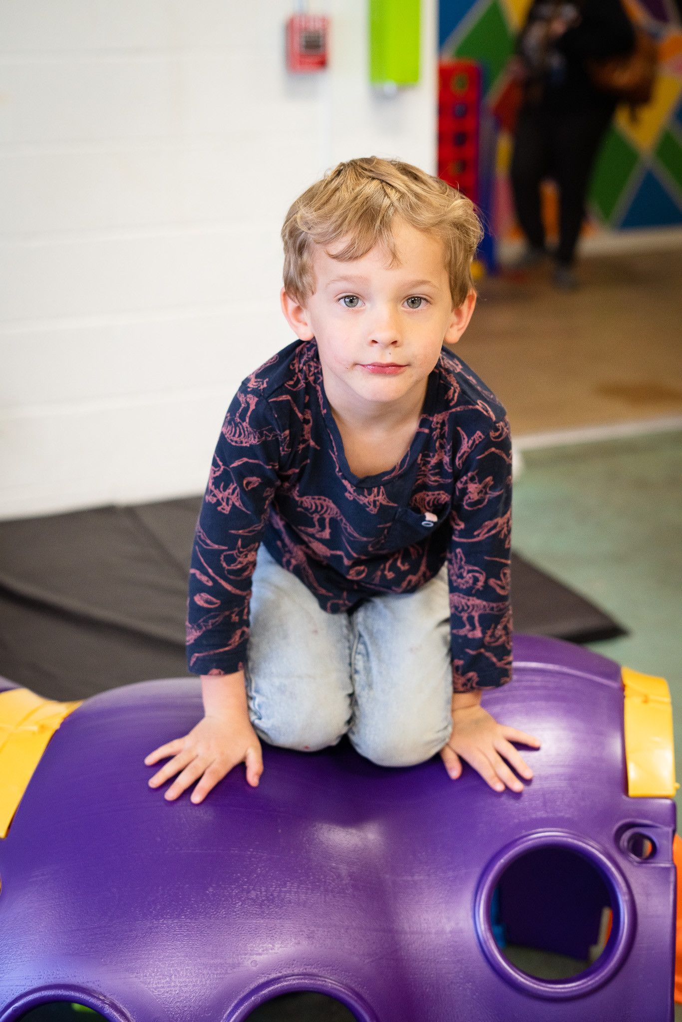 A young boy is kneeling on top of a purple toy in a playground.