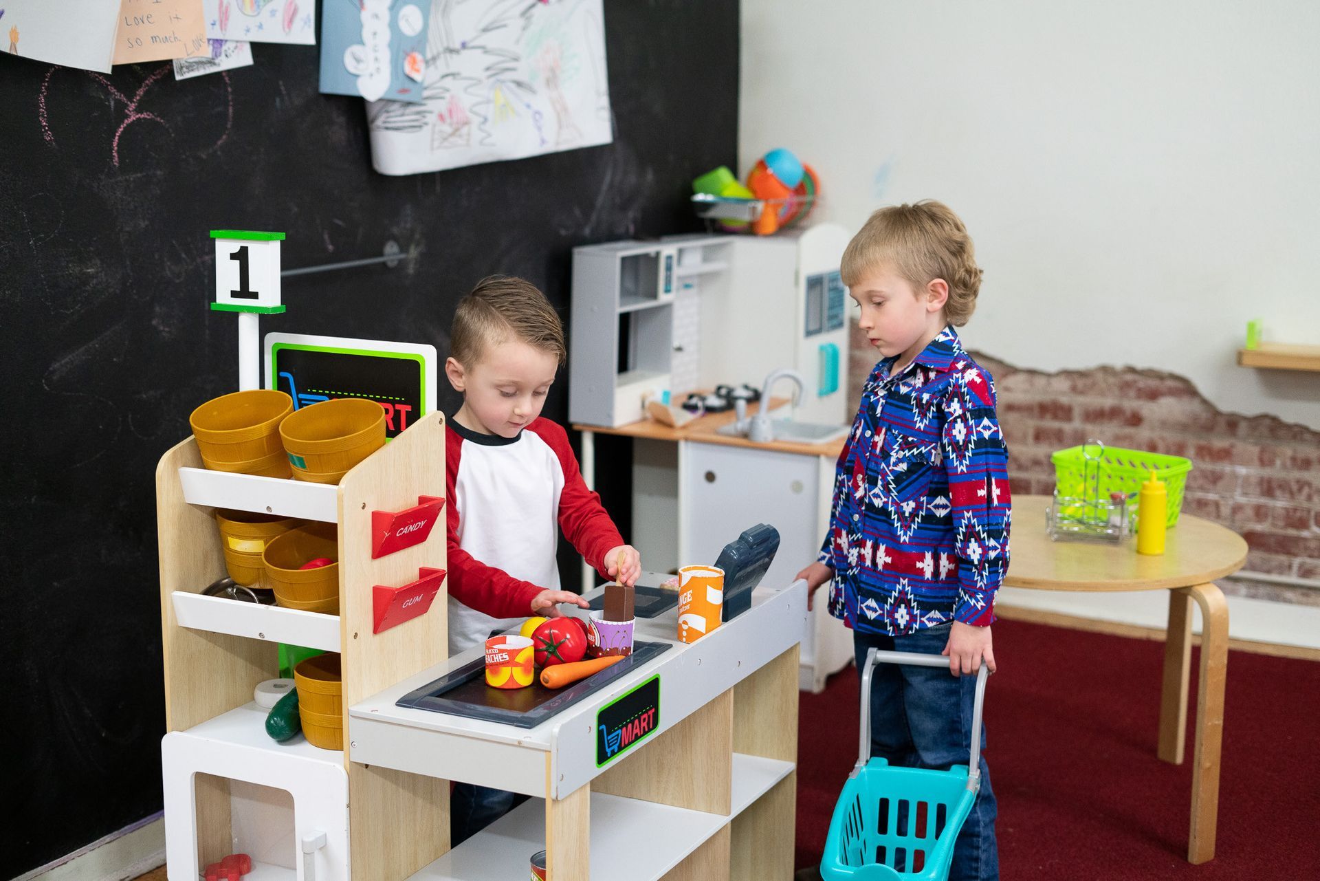 Two young boys are playing with a toy kitchen in a play room.