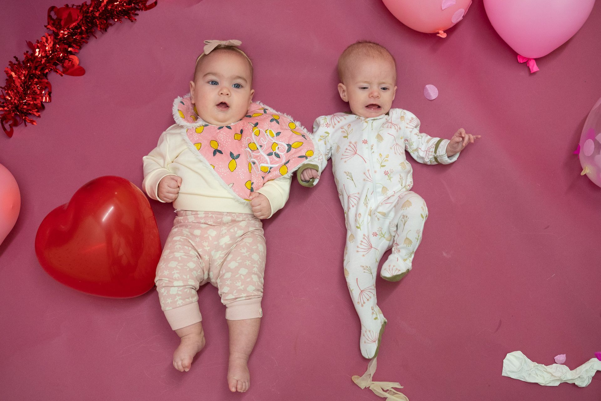 Two babies are laying next to each other on a pink blanket.