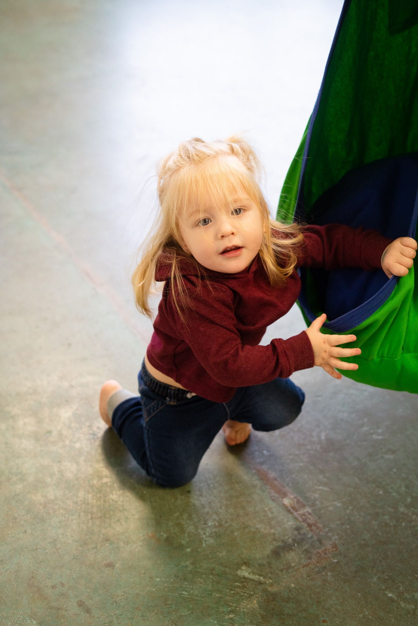 A little girl is playing in a green hammock on the floor.