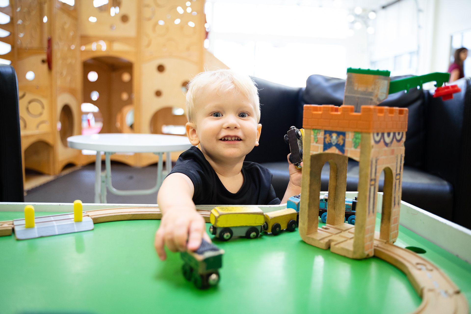 A little boy is playing with a wooden train set on a table.