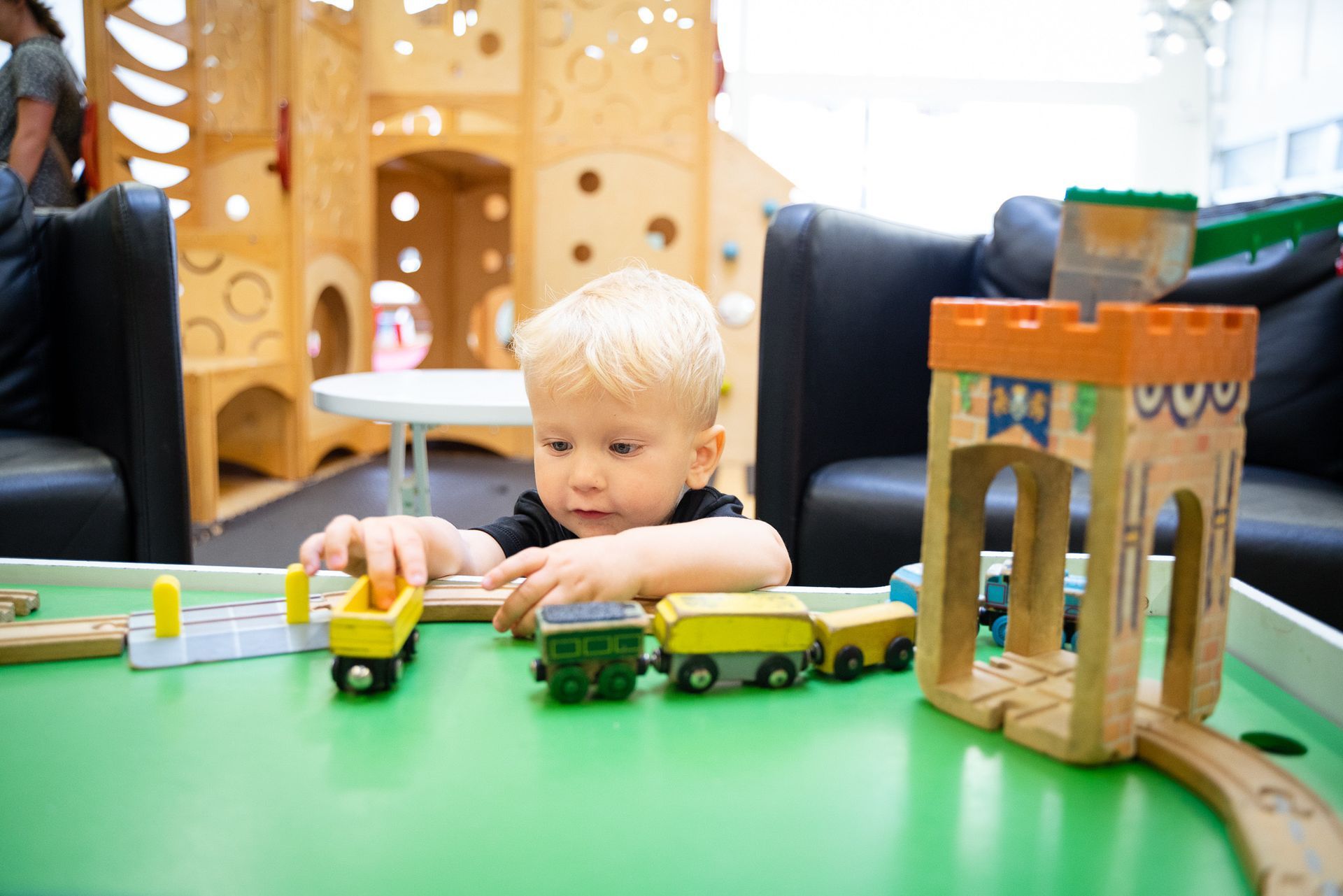 A young boy is playing with a wooden train set on a table.