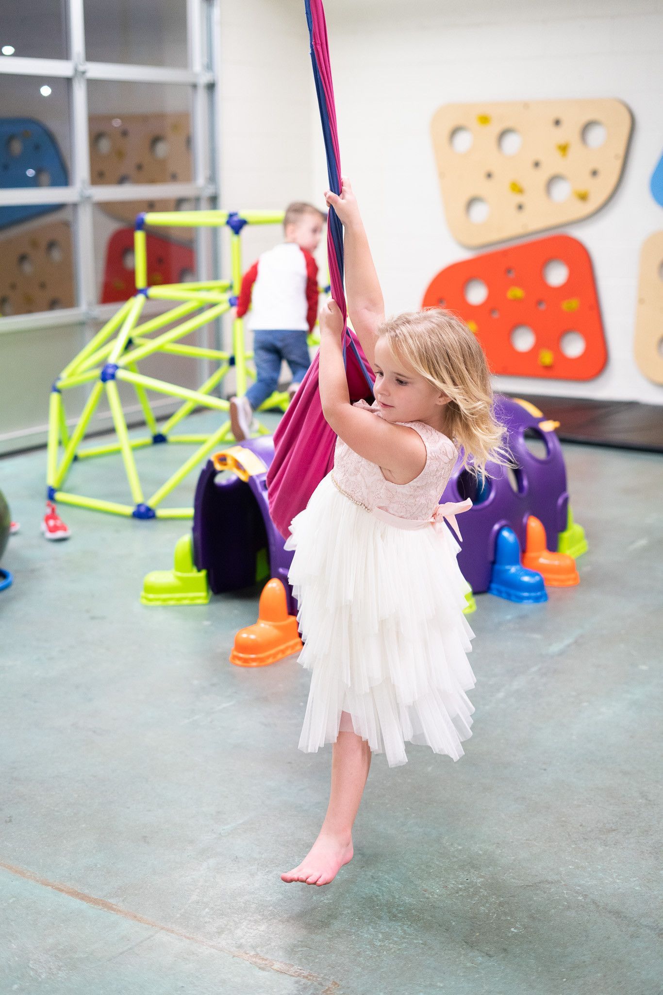 A little girl in a white dress is playing on a swing in a playground.